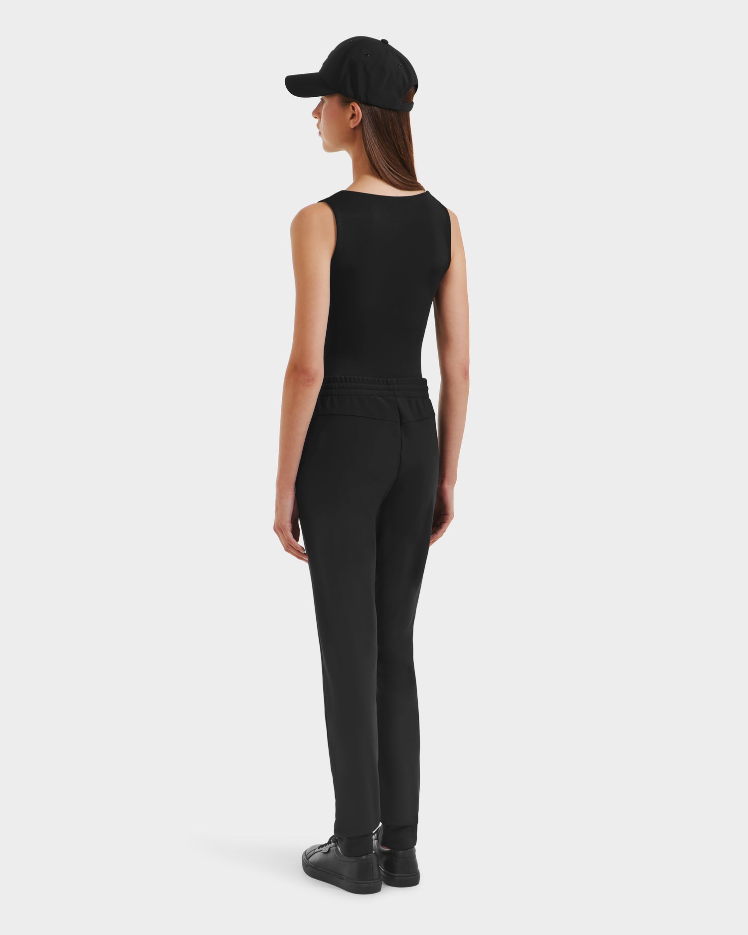 A woman models the Rudsak DAMERIS - 8525575 Black joggers, paired with a black cap, sleeveless top, and shoes, shown from the back against a plain white background.