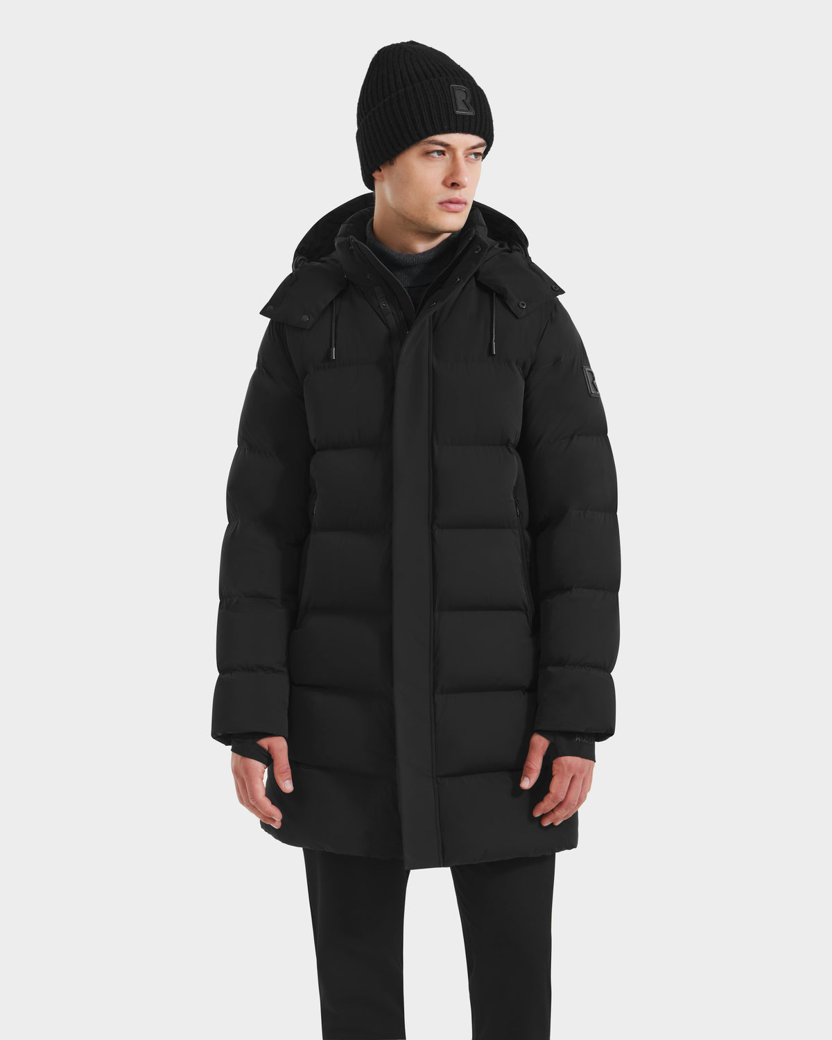 A man wearing the Rudsak DAO - 6124604 Black, a mens mid-length puffer coat featuring a weather-resistant shell.