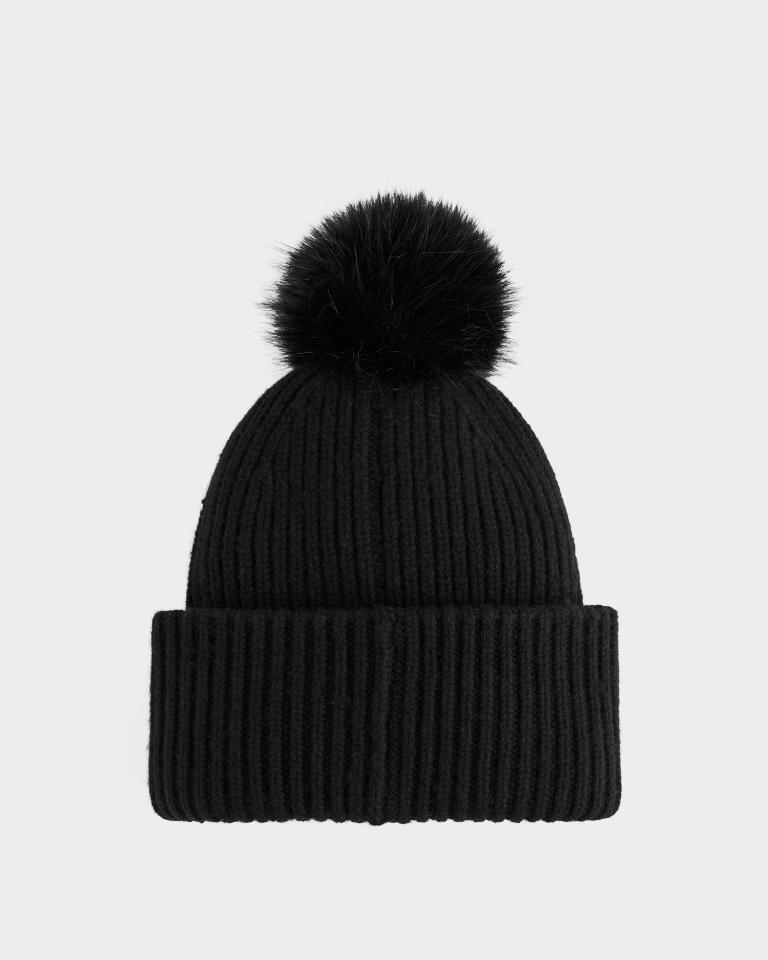 The Rudsak DARA - 8425019 Black is a women’s black knit tuque featuring a wide folded brim and a large faux fur pom pom, shown against a plain light gray background.