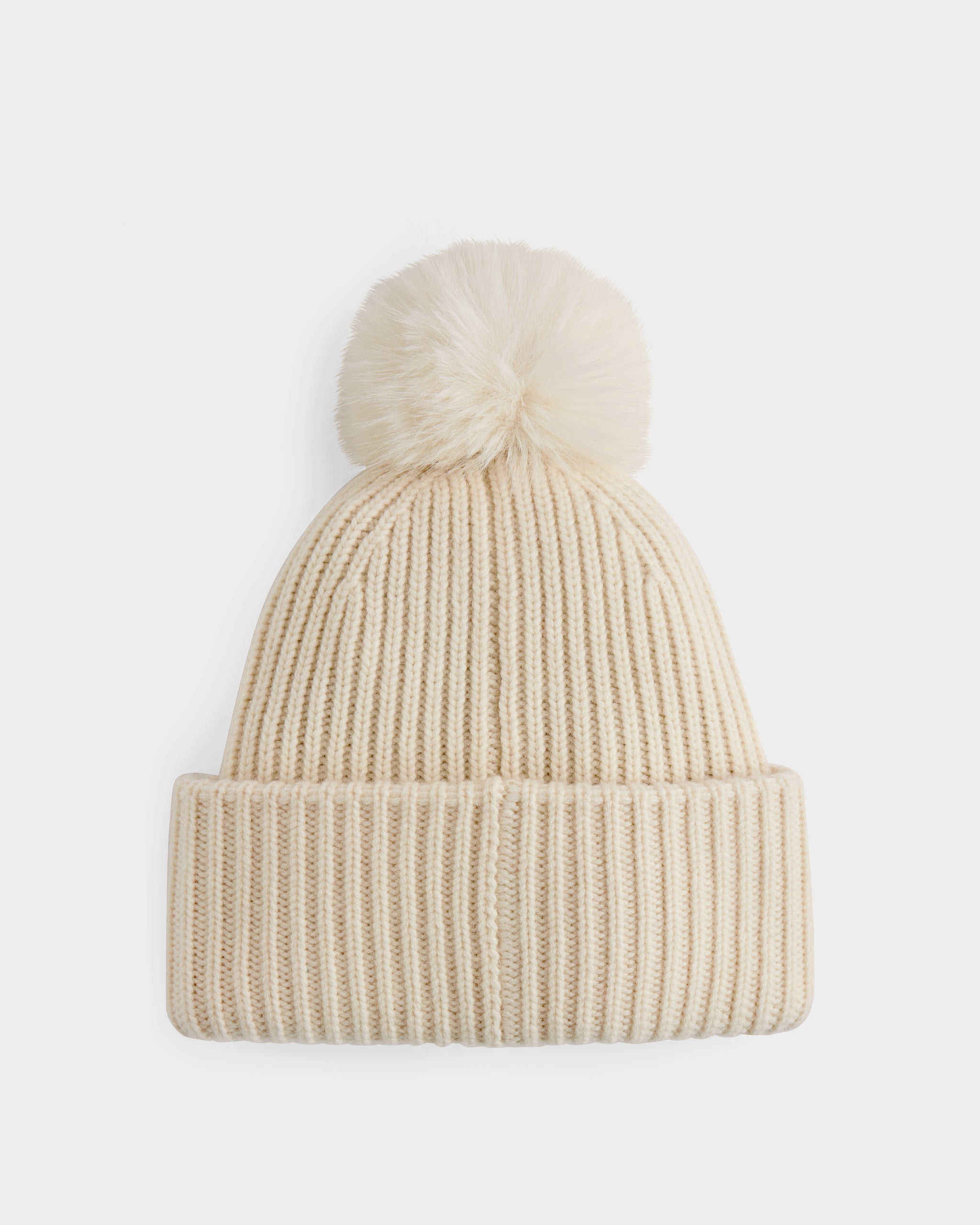 The Rudsak DARA - 8425019 Vanilla is a cream knit beanie with a folded brim and a large faux fur pom pom, shown against a white background—a stylish cold-weather essential.