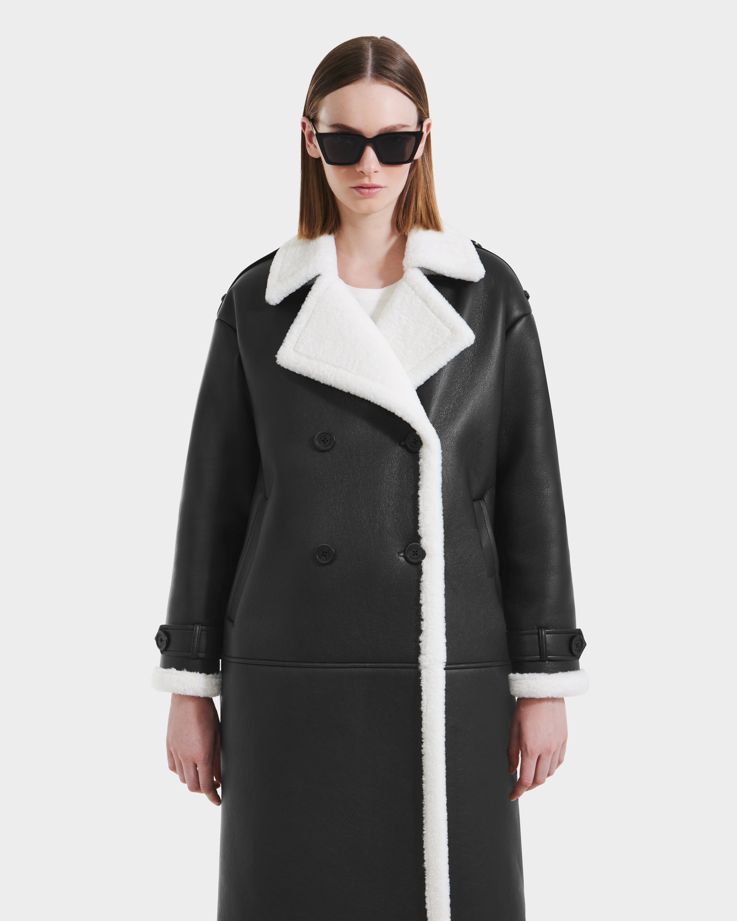 A person models the Rudsak DARCY - L125539 Black women's faux sherpa coat with white trim, standing against a plain white background and looking straight ahead with a neutral expression.
