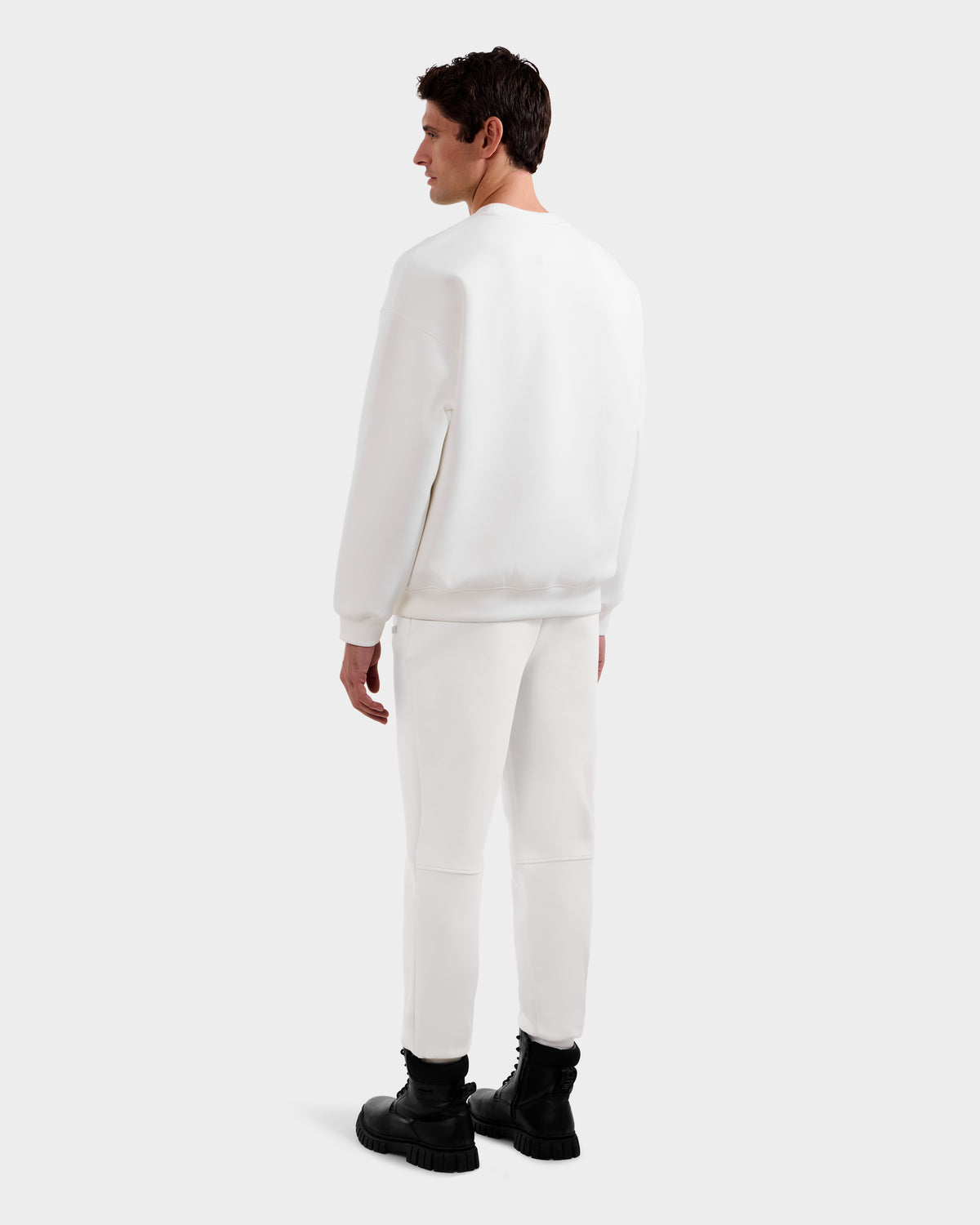 A man faces away, wearing the DECLAN - 6525648 Iceland crewneck sweatshirt by Rudsak with matching white pants and black lace-up boots, set against a plain light gray background.