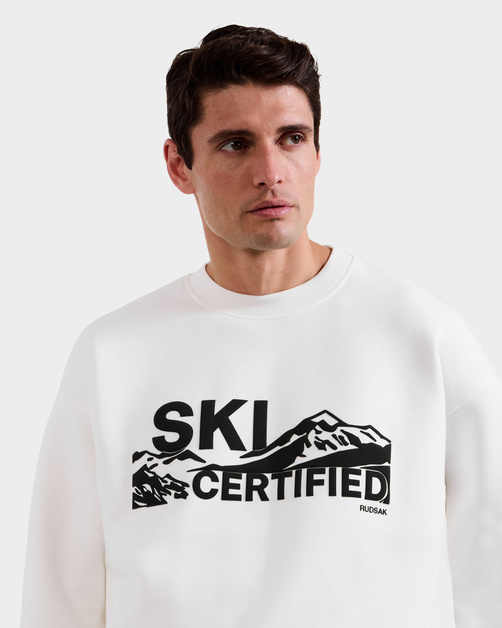 Model wears the Rudsak DECLAN - 6525648 Iceland men’s crewneck sweatshirt, featuring a black mountain graphic and "SKI CERTIFIED" text on the front, turning slightly to his right to highlight this stylish piece.