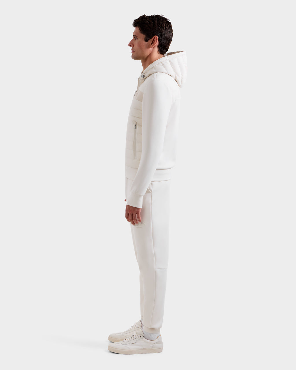 A man in profile, facing left, wears the Rudsak DEE MP - 6125673 Vanilla lightweight down jacket with waterproof zippers, matching pants, and white sneakers against a plain white background.