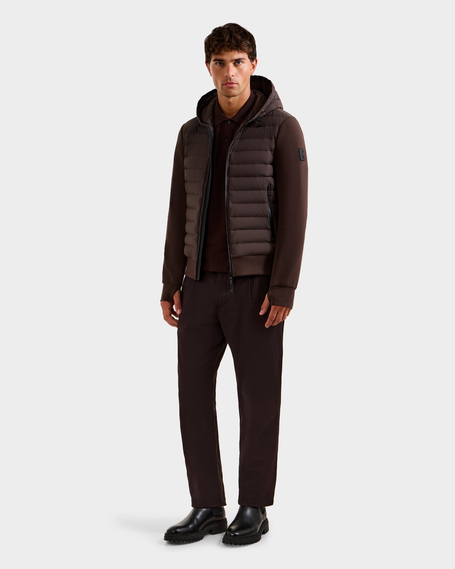 A man stands against a plain background, wearing the Rudsak DEE MAT - 6124028 Espresso lightweight down jacket with matching brown pants and black shoes, looking directly at the camera with a neutral expression.