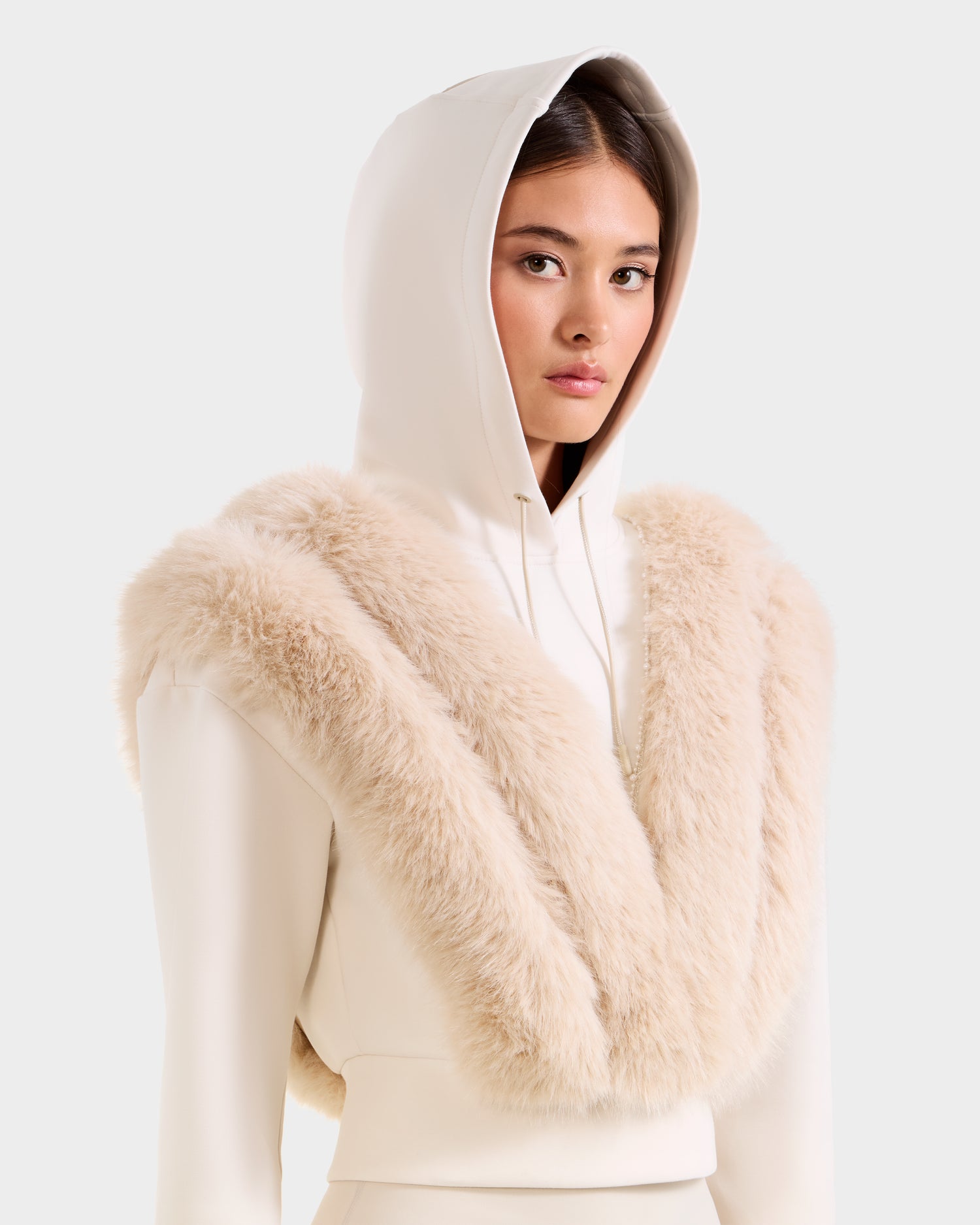 A woman in a Rudsak DELLA - 8525668 Vanilla white cropped hoodie and a cream faux fur scarf poses against a plain light background.