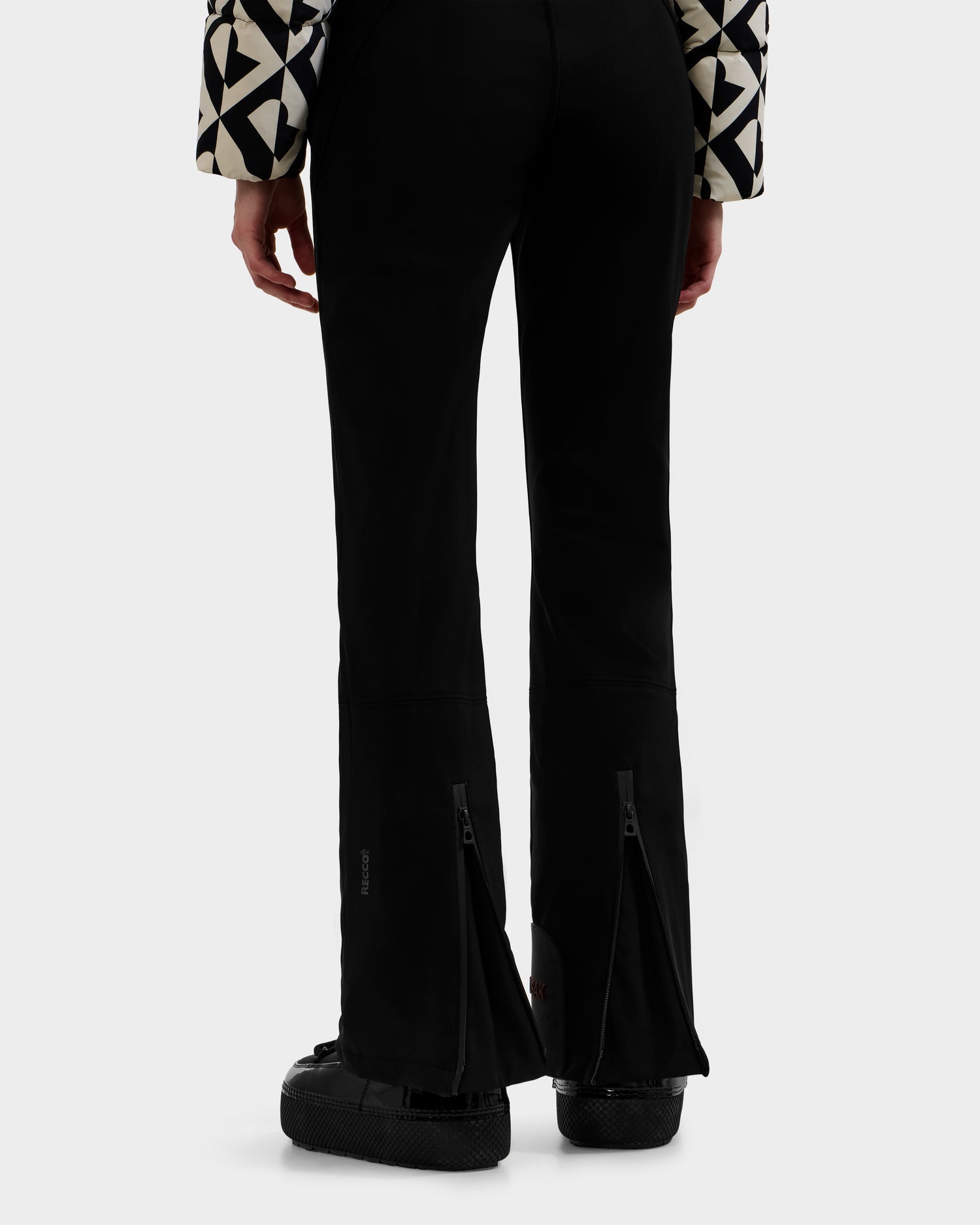 A person, shown from the waist down and viewed from behind, wears Rudsak’s DINARA - 8125600 Vanilla Monogram top with black flared pants featuring rear zippers and chunky black shoes—a look echoing bold women’s ski suit style.
