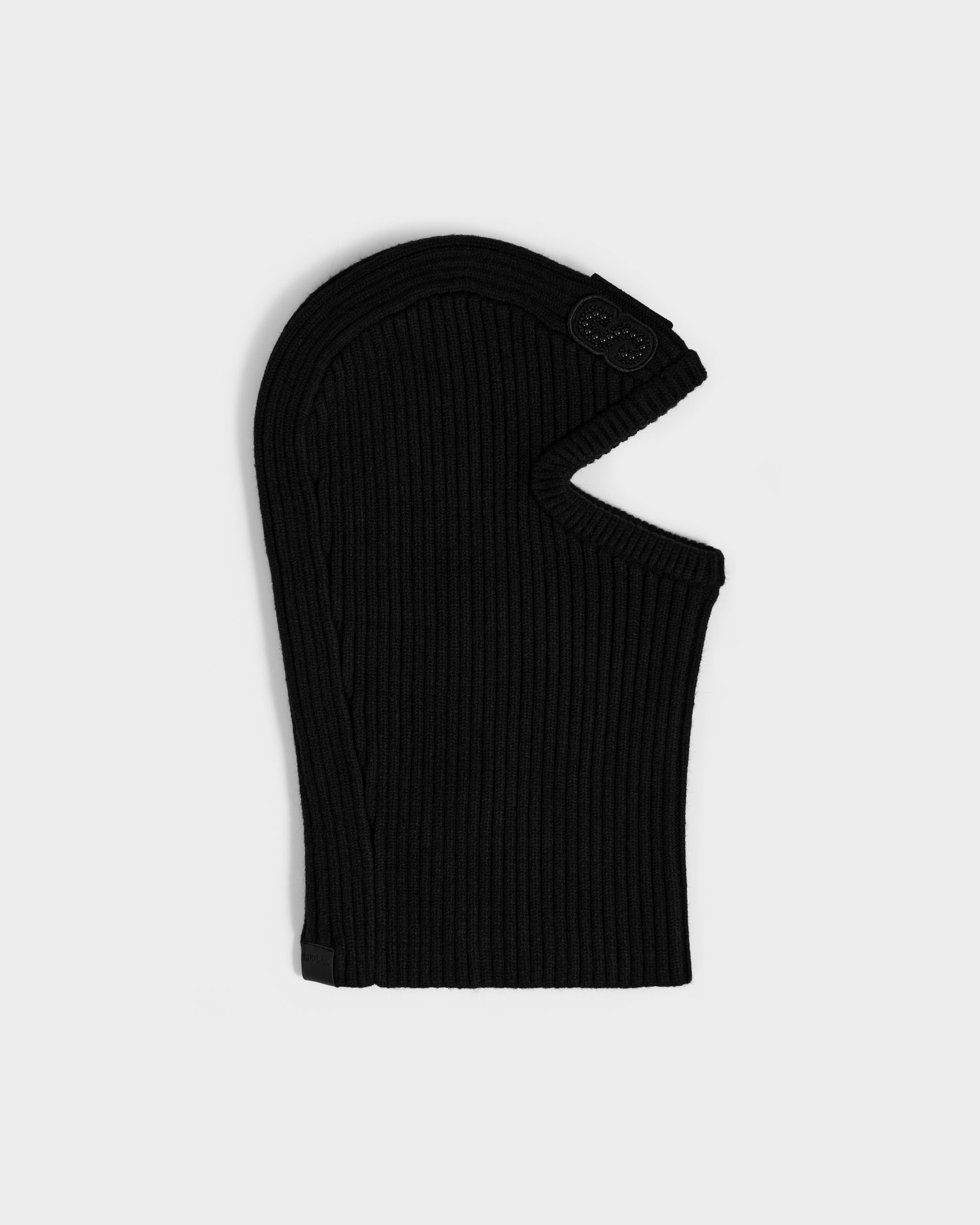 The DIXIE - 8425551 Black by Rudsak is a ribbed women's fitted knit balaclava with a face opening and a patch detail near the forehead, shown on a plain light gray background—perfect for your winter wardrobe.