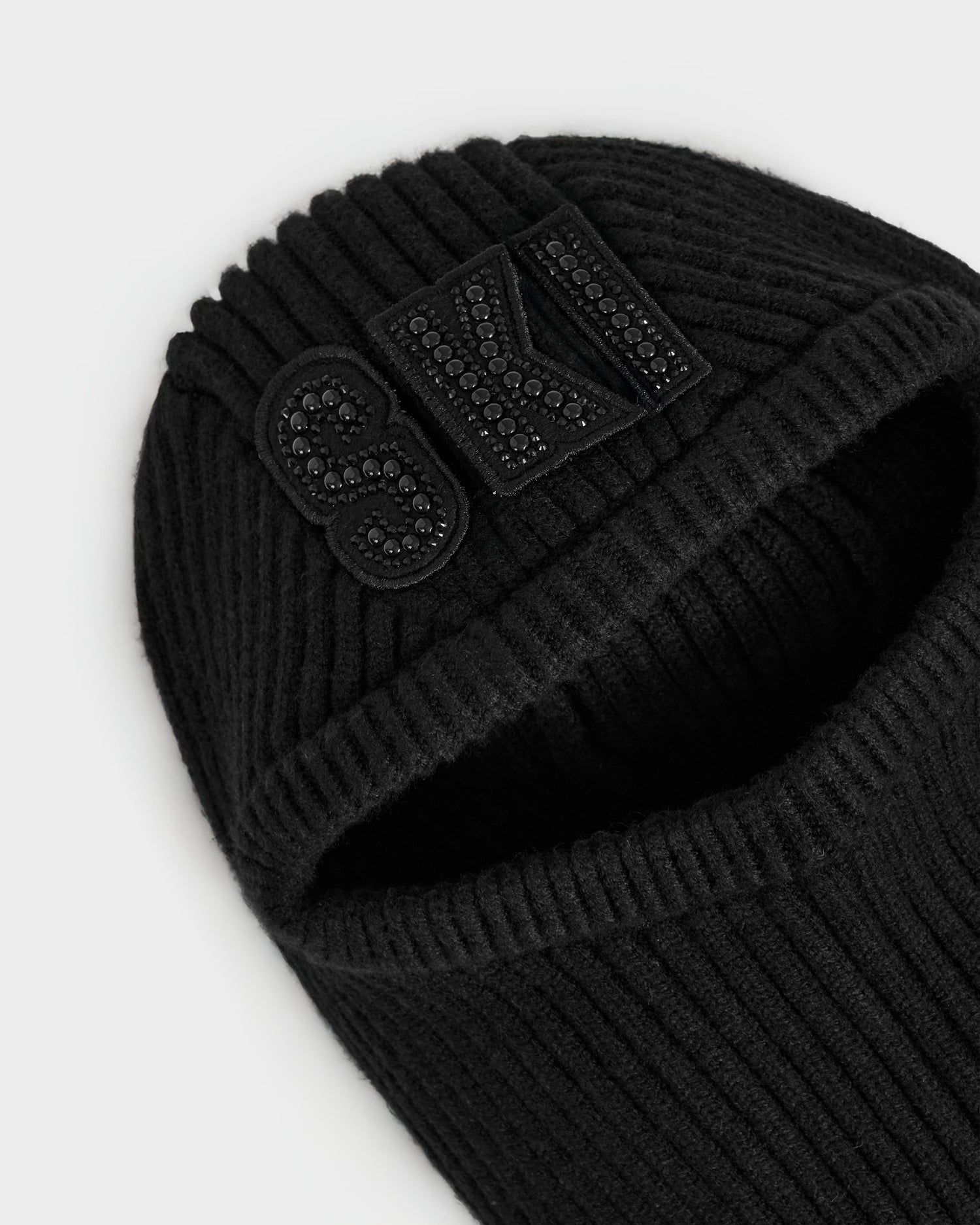The DIXIE - 8425551 Black by Rudsak is a women's fitted black ribbed knit balaclava with a large face opening and a crystal-embellished SKI logo—ideal for elevating your winter style.