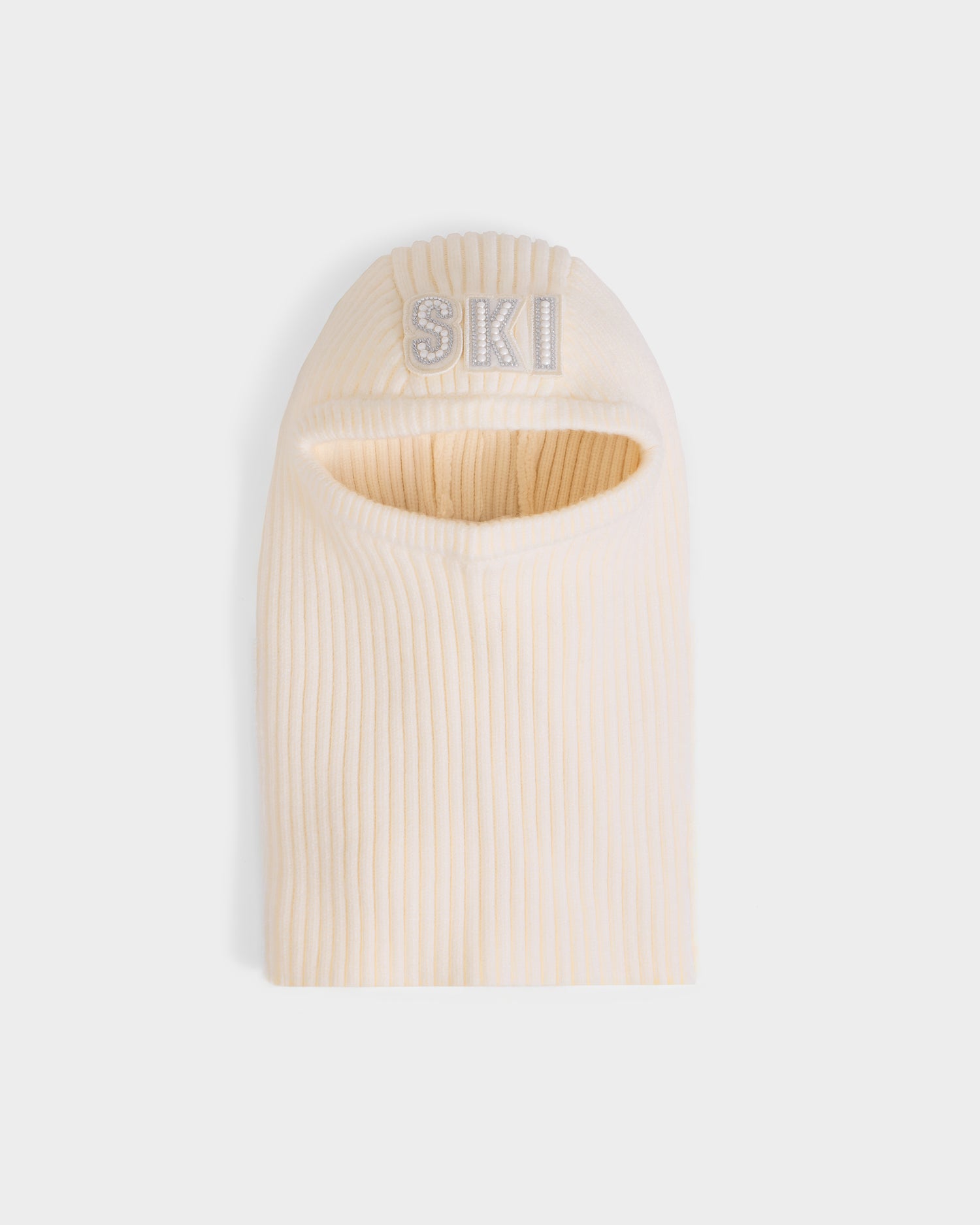 The DIXIE - 8425551 Vanilla by Rudsak is a cream-colored women’s knit balaclava with a ribbed design, oval face opening, and SKI embroidered in white on the forehead—an essential winter accessory, shown against a plain light gray background.