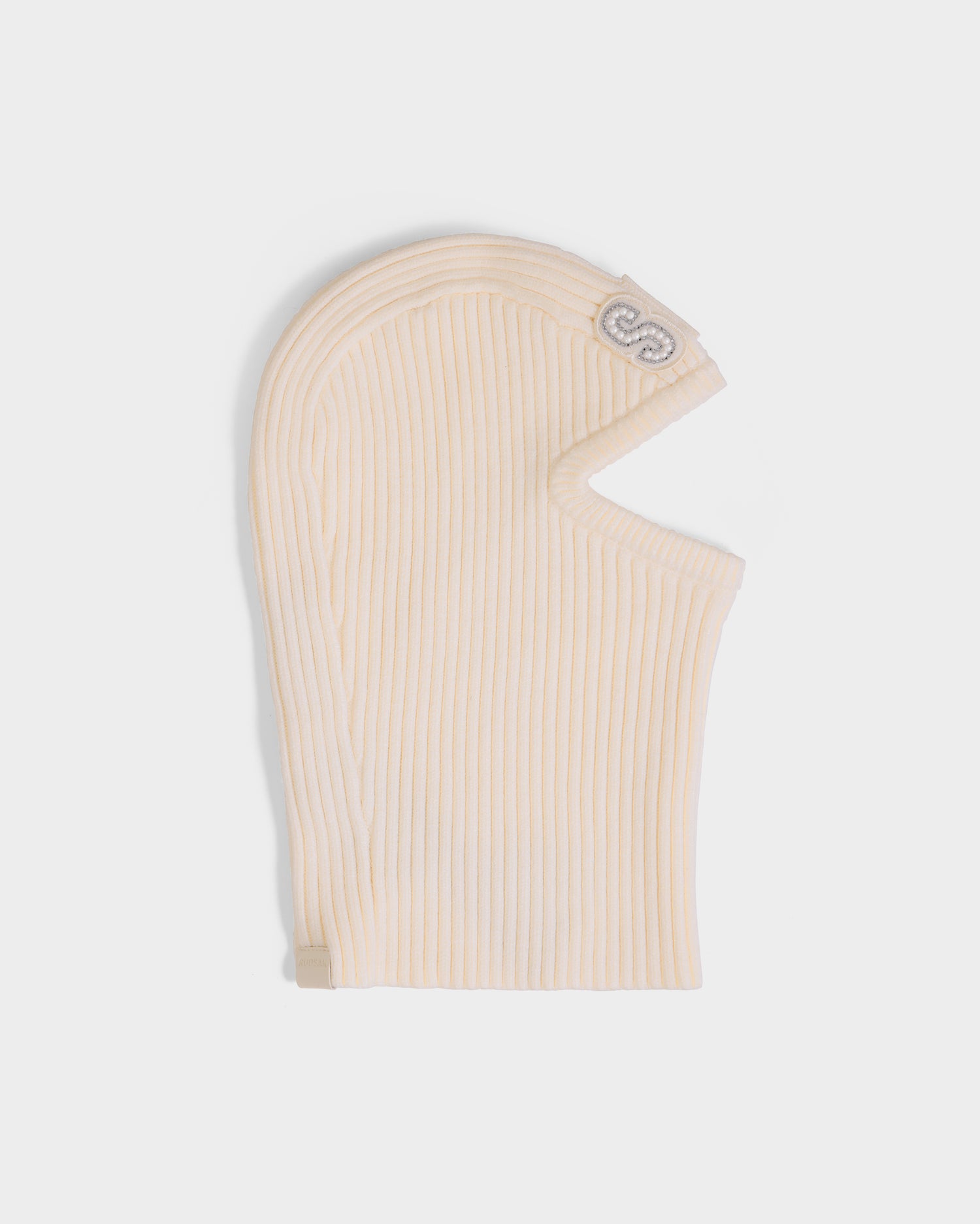 The DIXIE - 8425551 Vanilla by Rudsak is a cream women’s knit balaclava with a ribbed texture, open face, and subtle side logo—shown flat on a white background for a cozy winter look.
