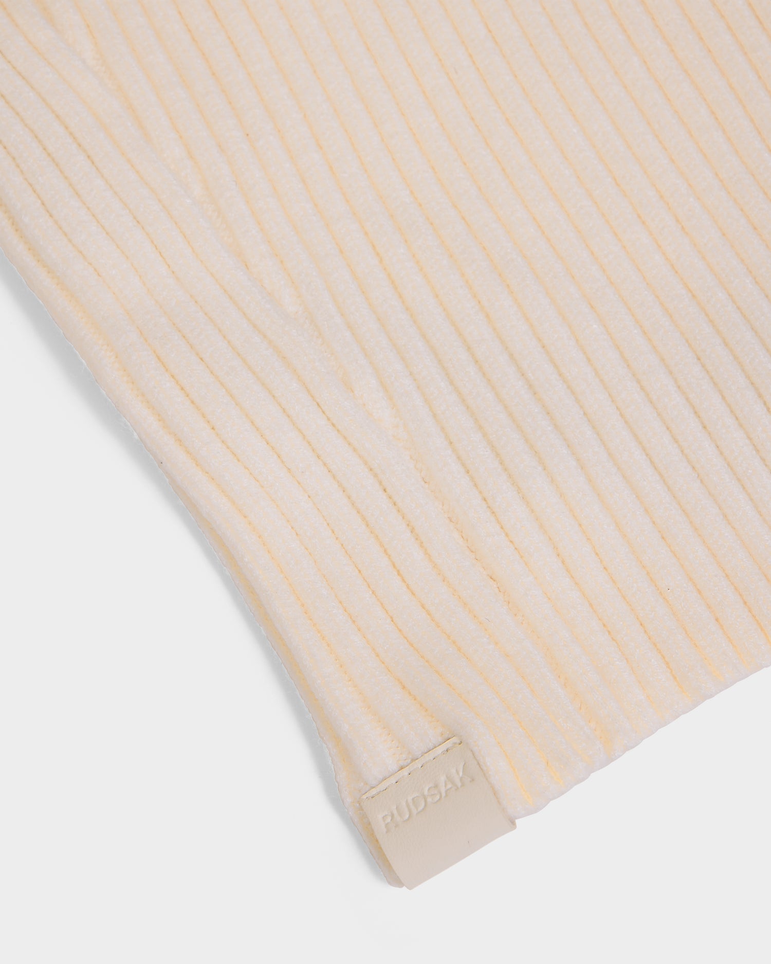 A close-up of the DIXIE - 8425551 Vanilla by Rudsak shows its beige ribbed knit, featuring a small rectangular RUDSAK tag—an ideal winter accessory to elevate your style.