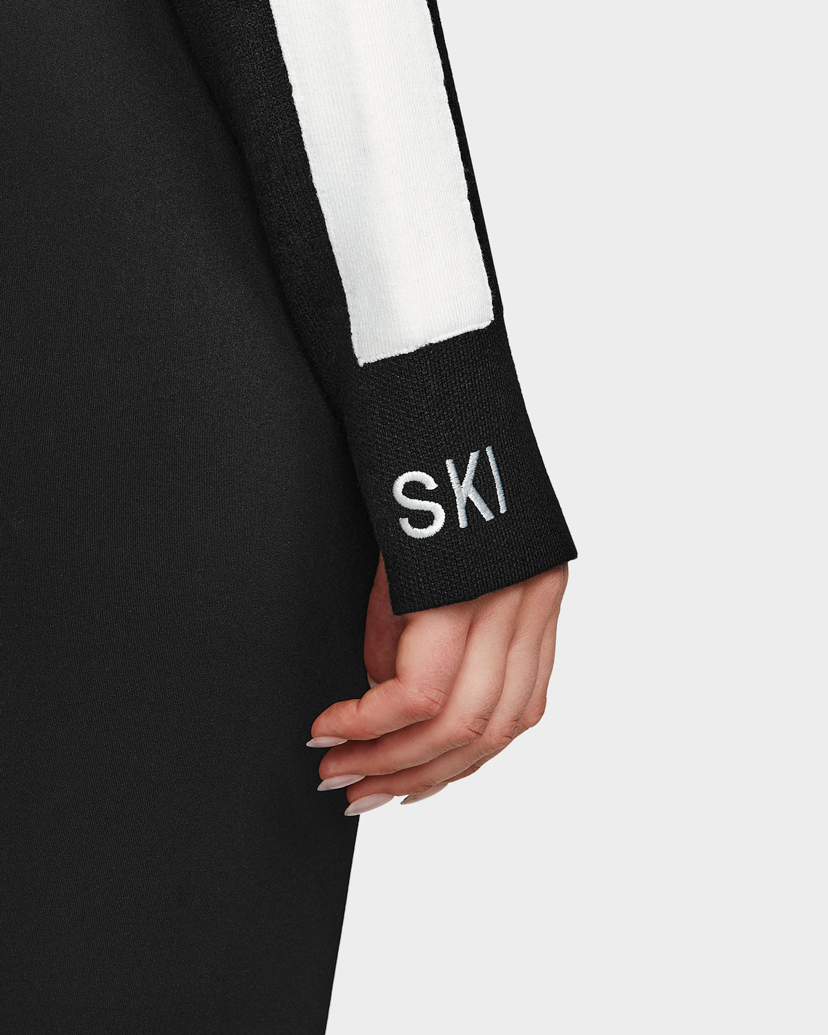 A close-up of a persons arm in the Rudsak ELIZABETH - 8524623 Black womens ski turtleneck, featuring SKI embroidery near the cuff and neatly manicured nails—an essential addition to your après-ski winter wardrobe.