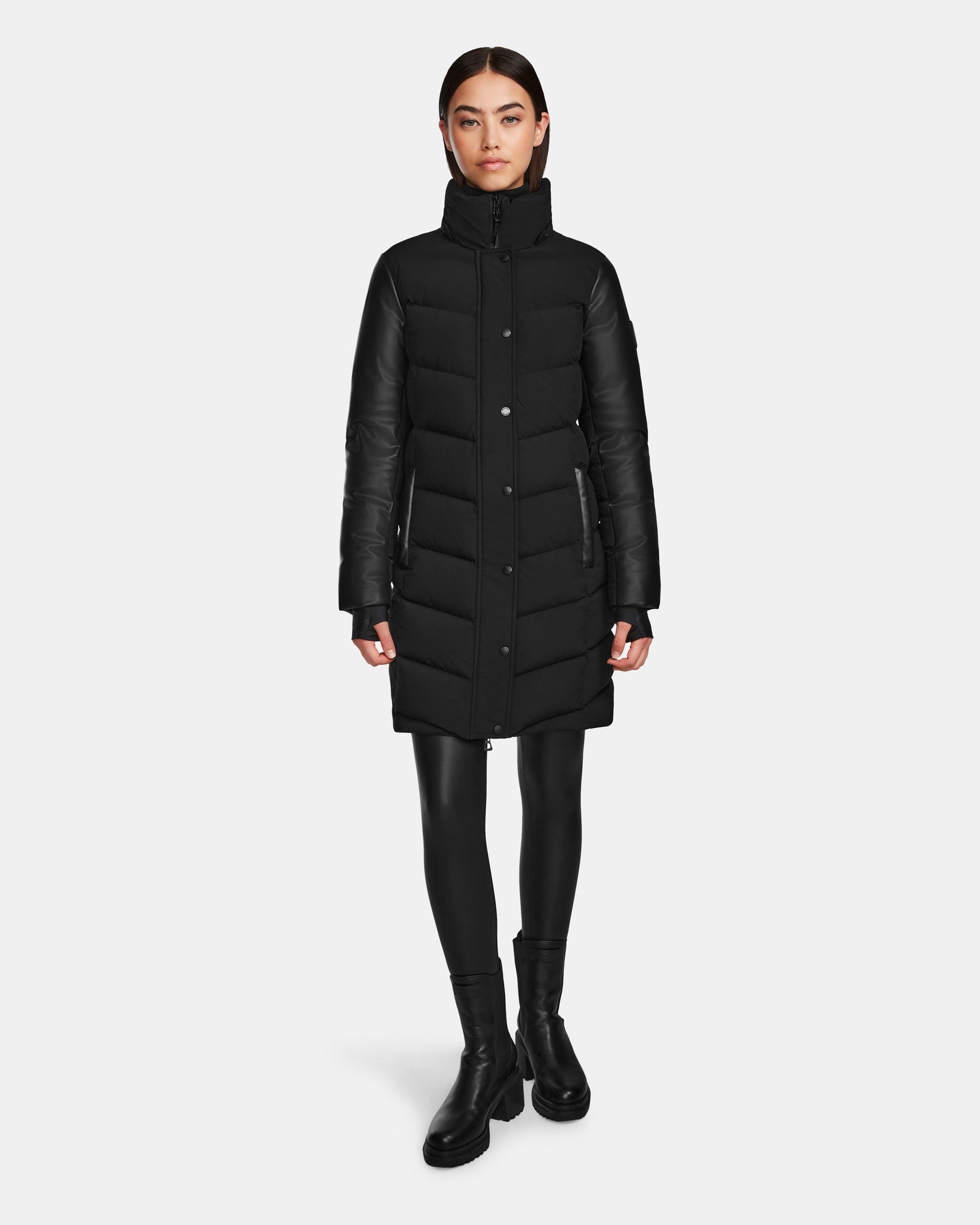 A woman stands facing forward, wearing the Rudsak ELSA - L123535 Black quilted down puffer, black leggings, and black ankle boots against a plain white background.