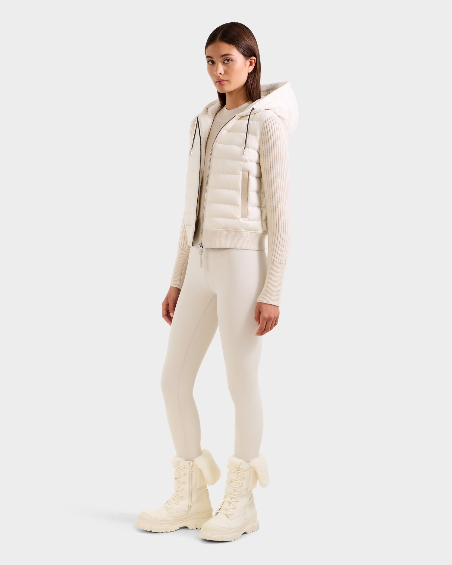 A woman stands in a neutral pose wearing the Rudsak EMILY - L125515 Vanilla off-white hooded down bomber jacket with matching fitted leggings and white lace-up winter boots, against a plain light background.