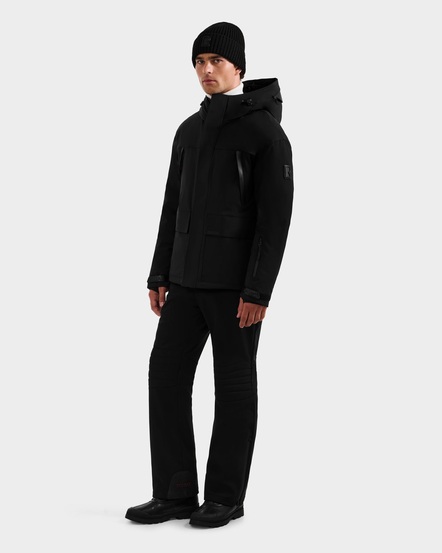 A person faces forward wearing the Rudsak ETHAN - 6125589 Black men’s ski jacket with RDS-certified down, paired with a black beanie, pants, and shoes against a plain white background.