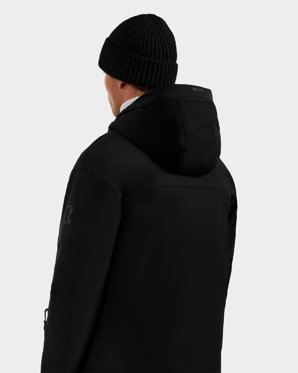A person is seen from the back wearing the Rudsak ETHAN - 6125589 Black men’s ski jacket and a black beanie against a plain, light gray background.