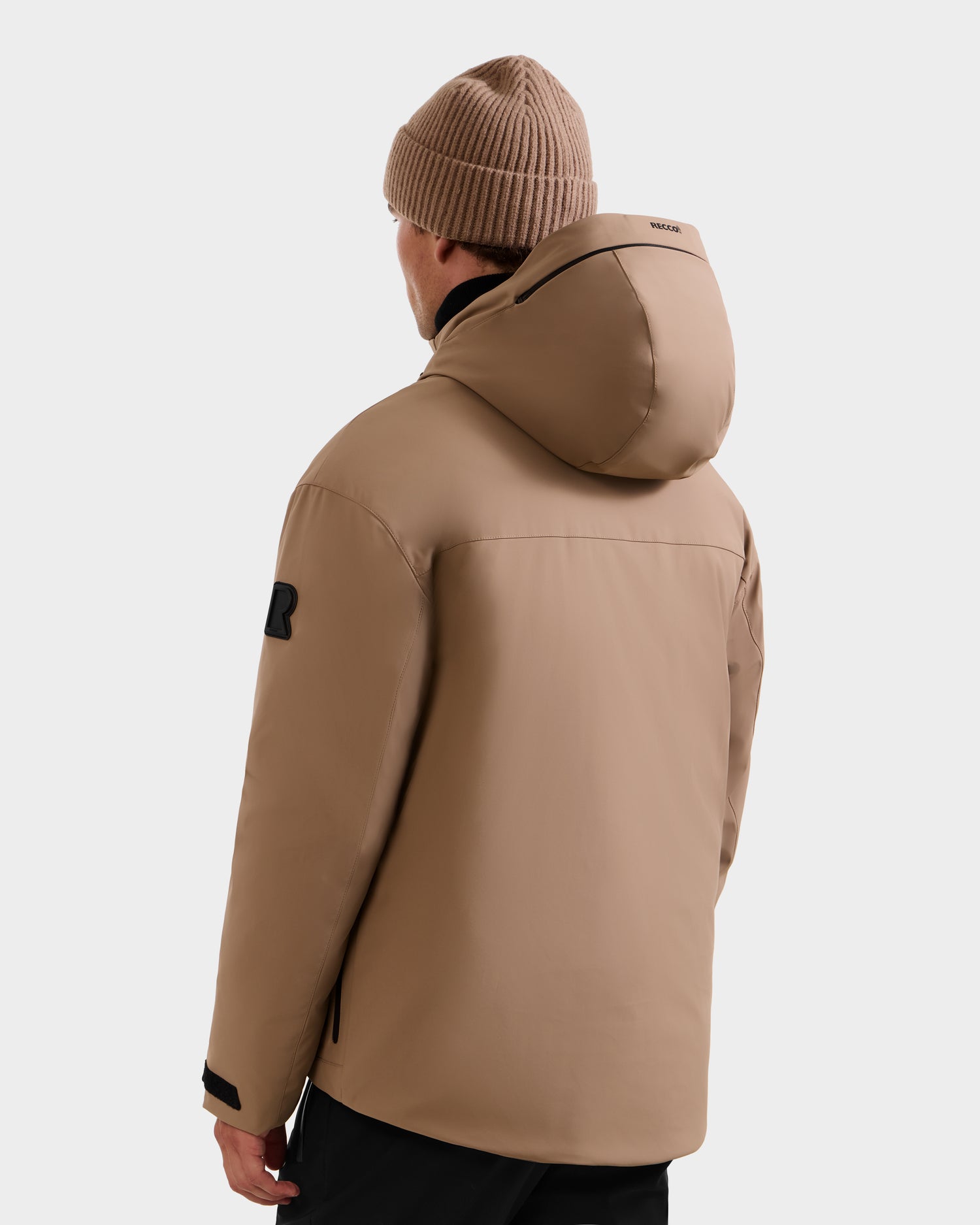 A person is seen from behind wearing the Rudsak ETHAN - 6125589 Sand men’s ski jacket with a matching knit beanie, standing against a plain light background.