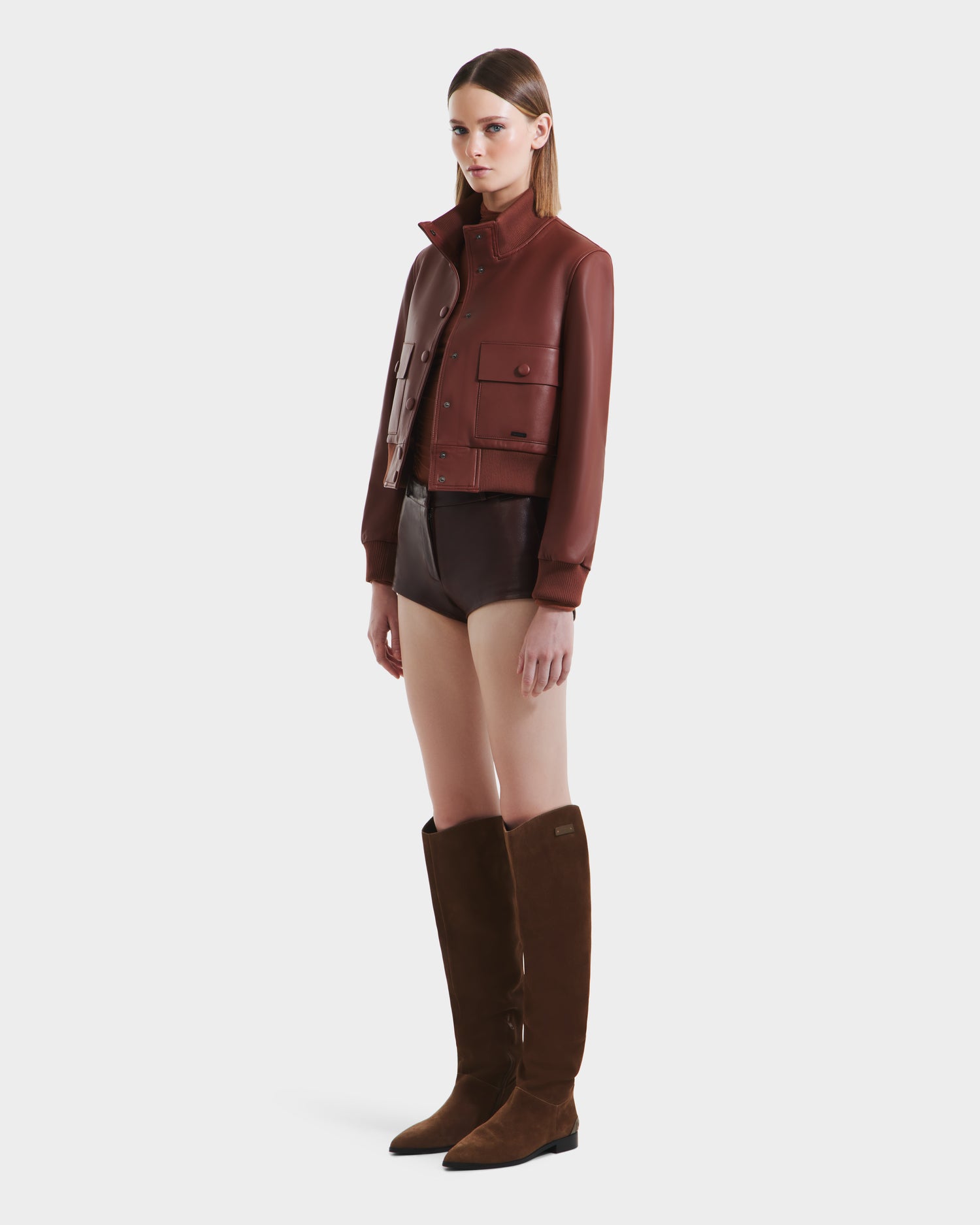 A woman in the EVERLEIGH - 8125547 Rust leather bomber jacket and shorts by Rudsak.