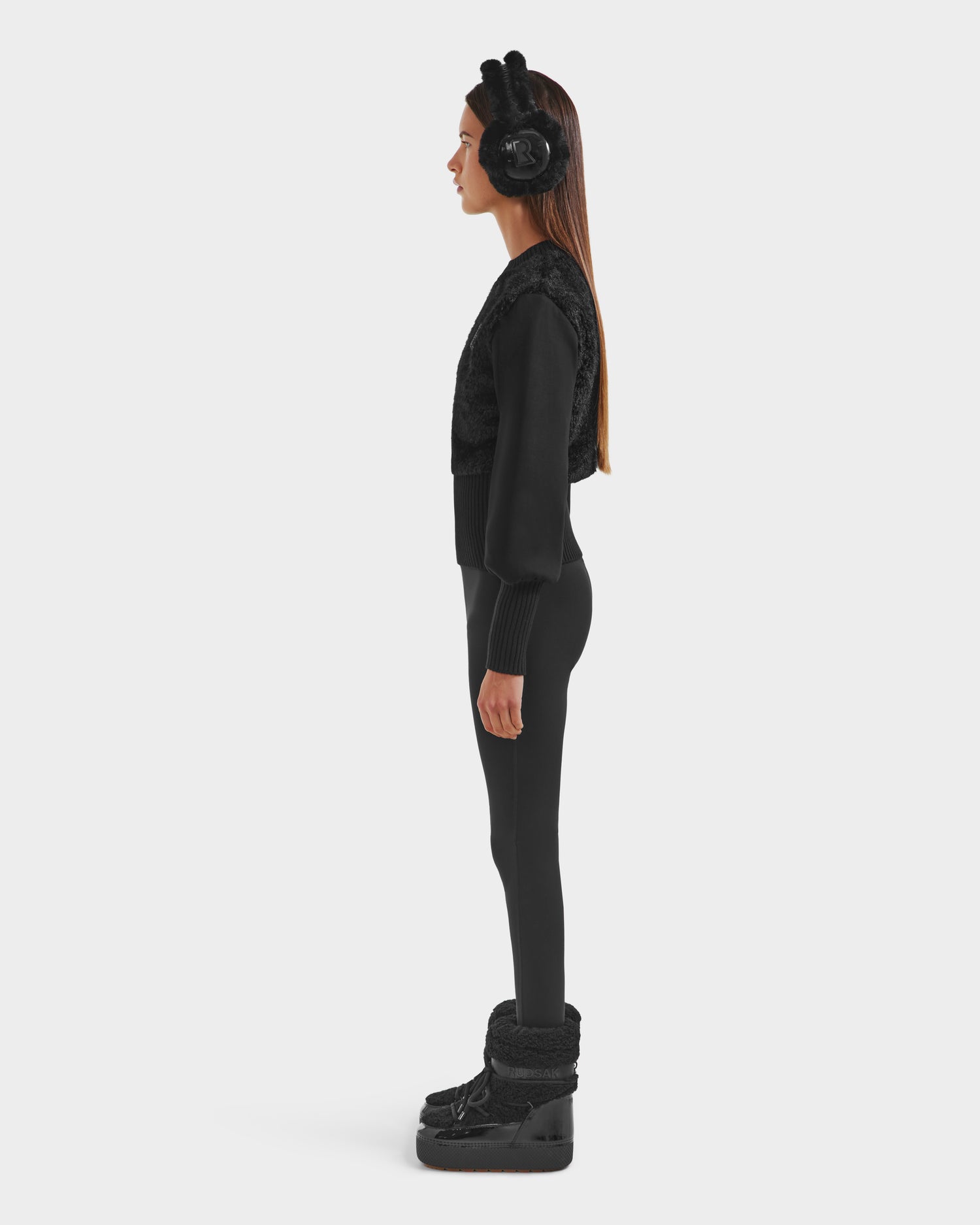 A woman stands in profile facing left, radiating cozy glamour in Rudsaks FLORENCE - 8525546 Black earmuffs with bear ears and a matching après-ski outfit against a plain white background.