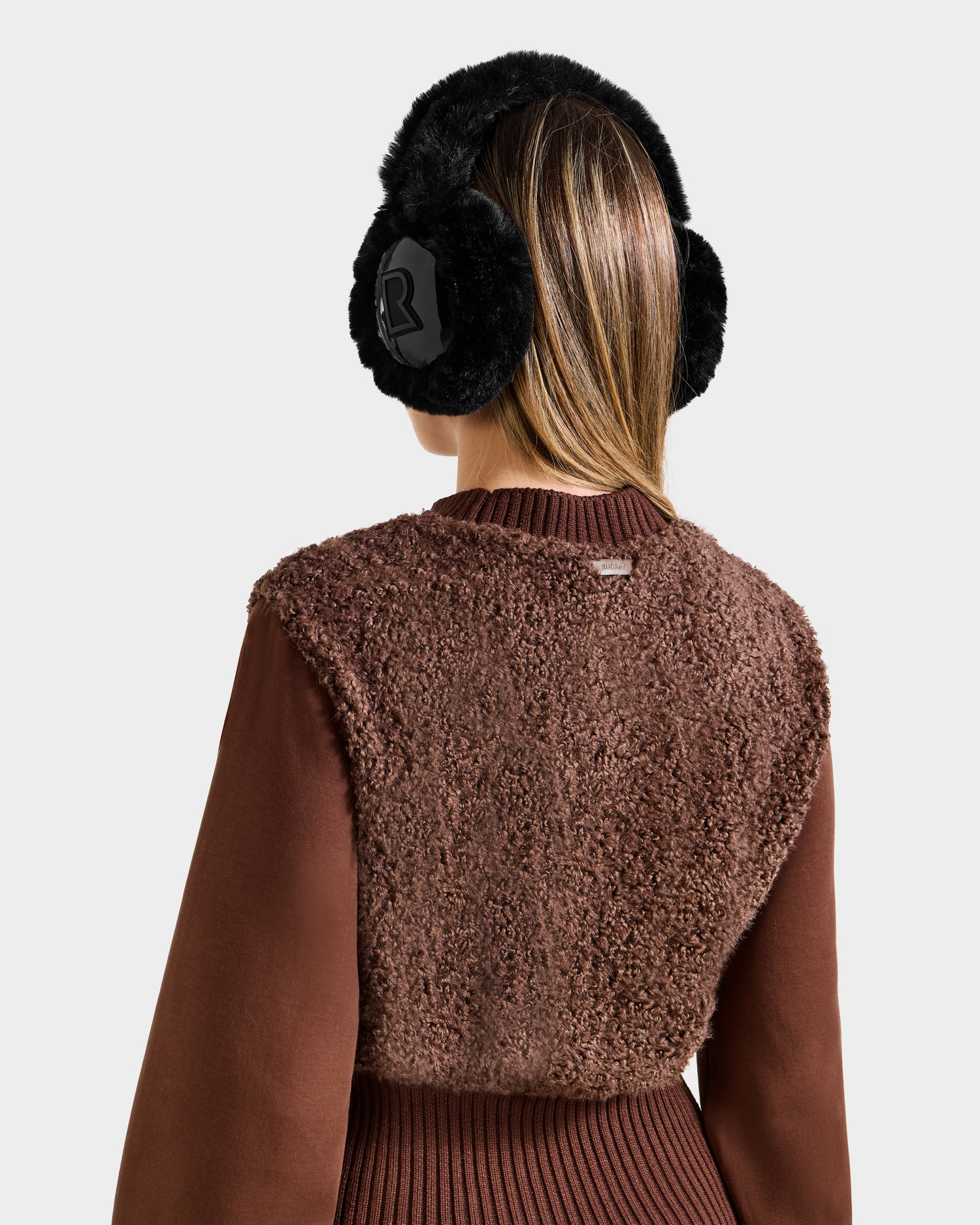 A person is seen from the back wearing the Rudsak FLORENCE - 8525546 Mocha top and black faux fur earmuffs, set against a plain light background.