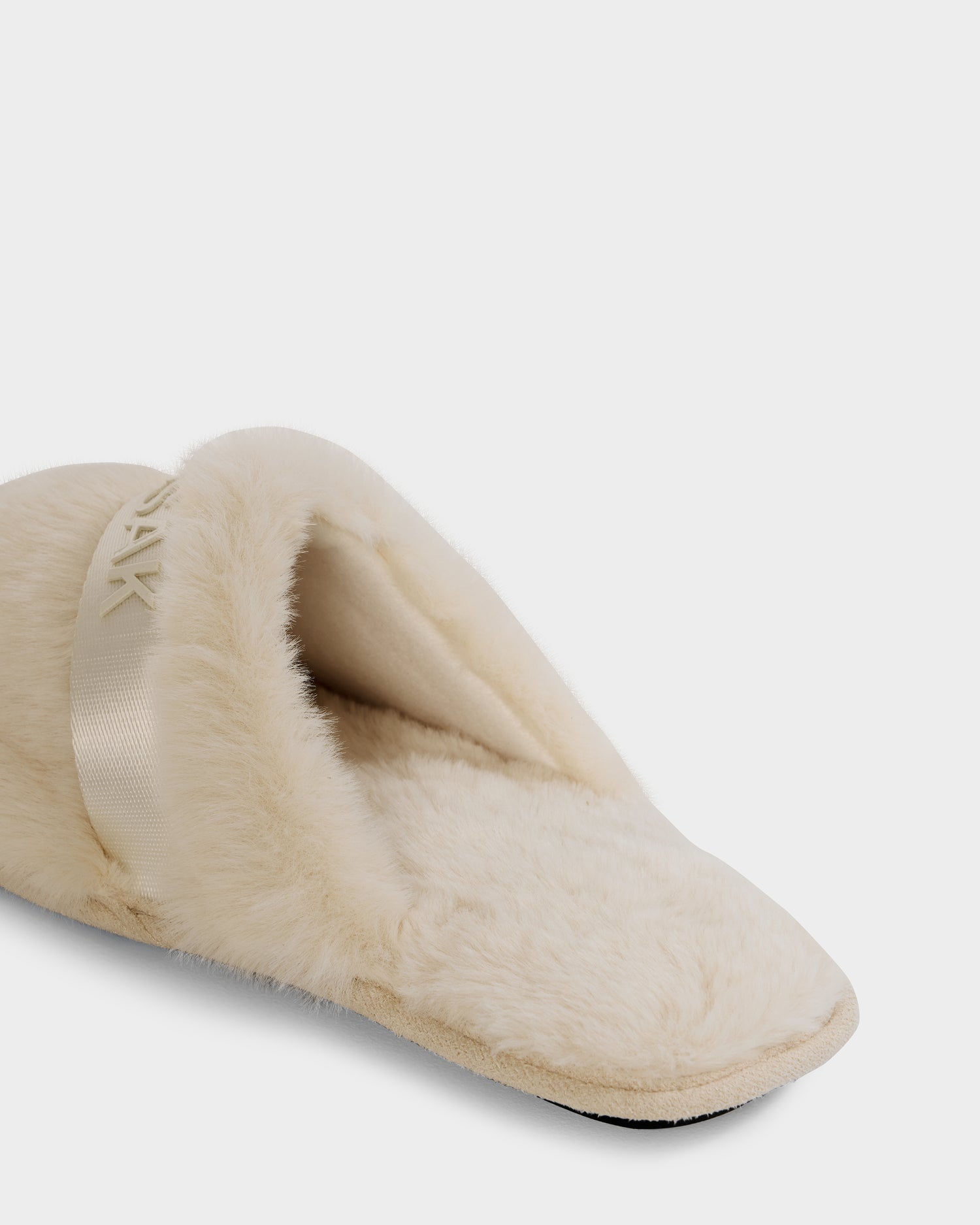 A close-up of the FLUFF - L223509 Cream women’s faux-fur slipper by Rudsak, featuring plush material, a satin band detail, and non-slip traction for cozy downtime—all shown on a white background.