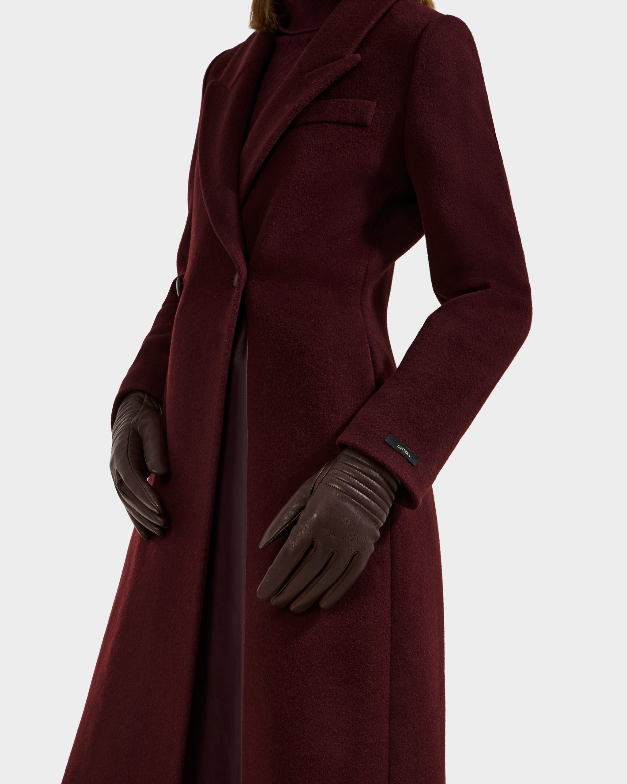 A person wearing the Rudsak GEMMA - 8425008 Espresso coat and cashmere-lined gloves stands against a white background; only the torso and upper legs are shown, spotlighting this elegant winter accessory.