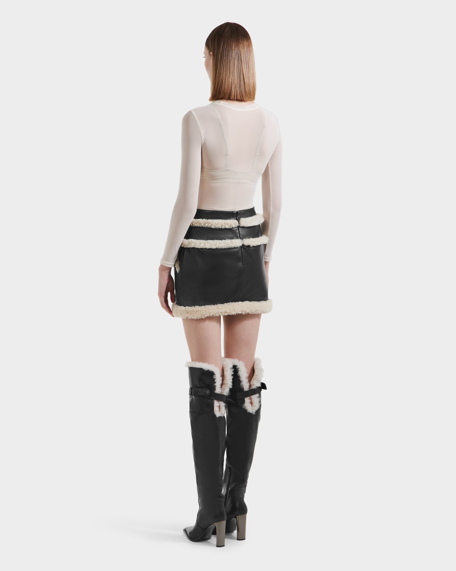 A woman wearing the Rudsak HAILEY - 8525609 Black leather mini skirt with shearling trim and boots.