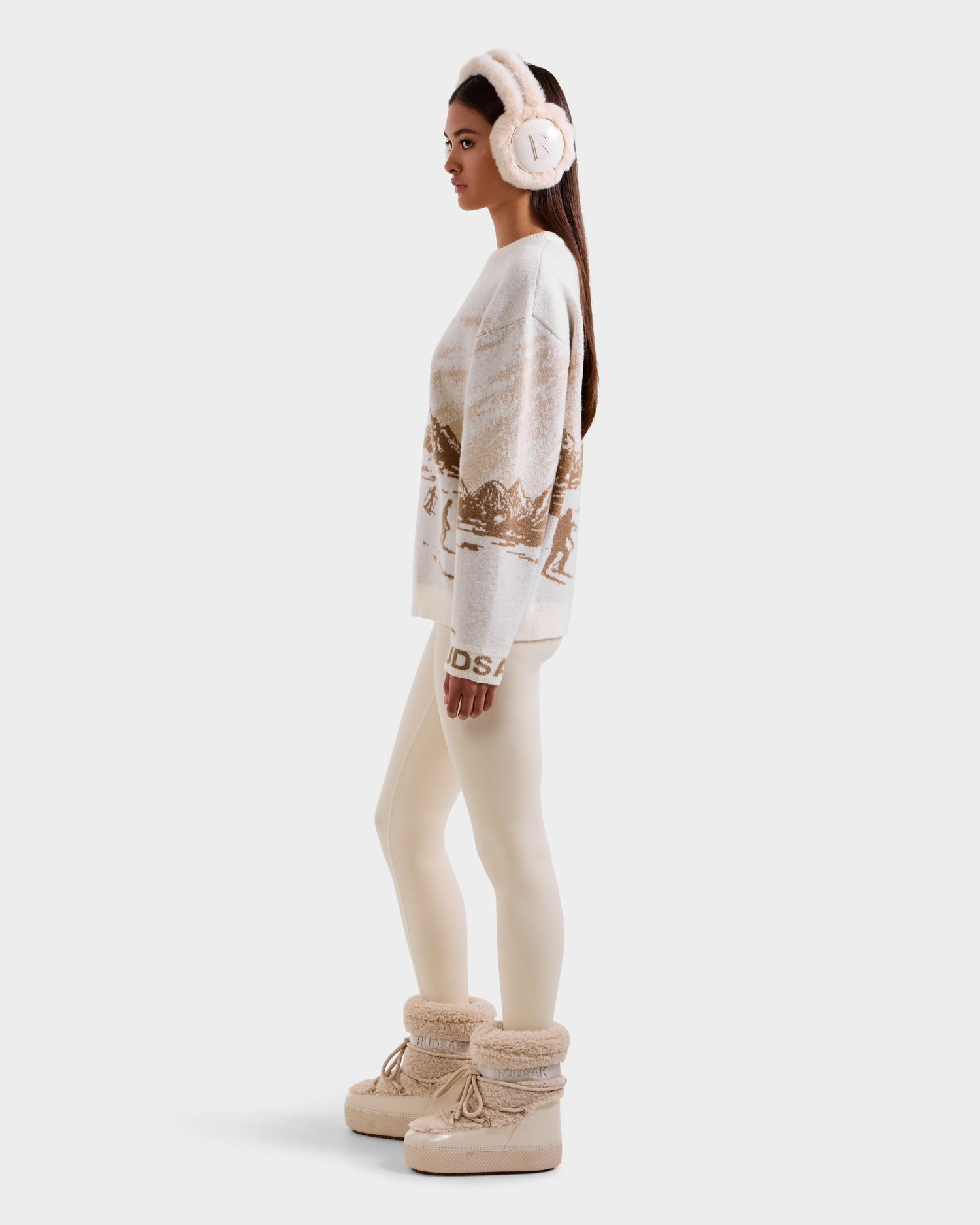 A woman in profile models the Rudsak IZZY - 9525557 Iceland W winter boots, featuring faux-fur trim, paired with an alpine crewneck sweater and ivory leggings, all set against a plain white background.