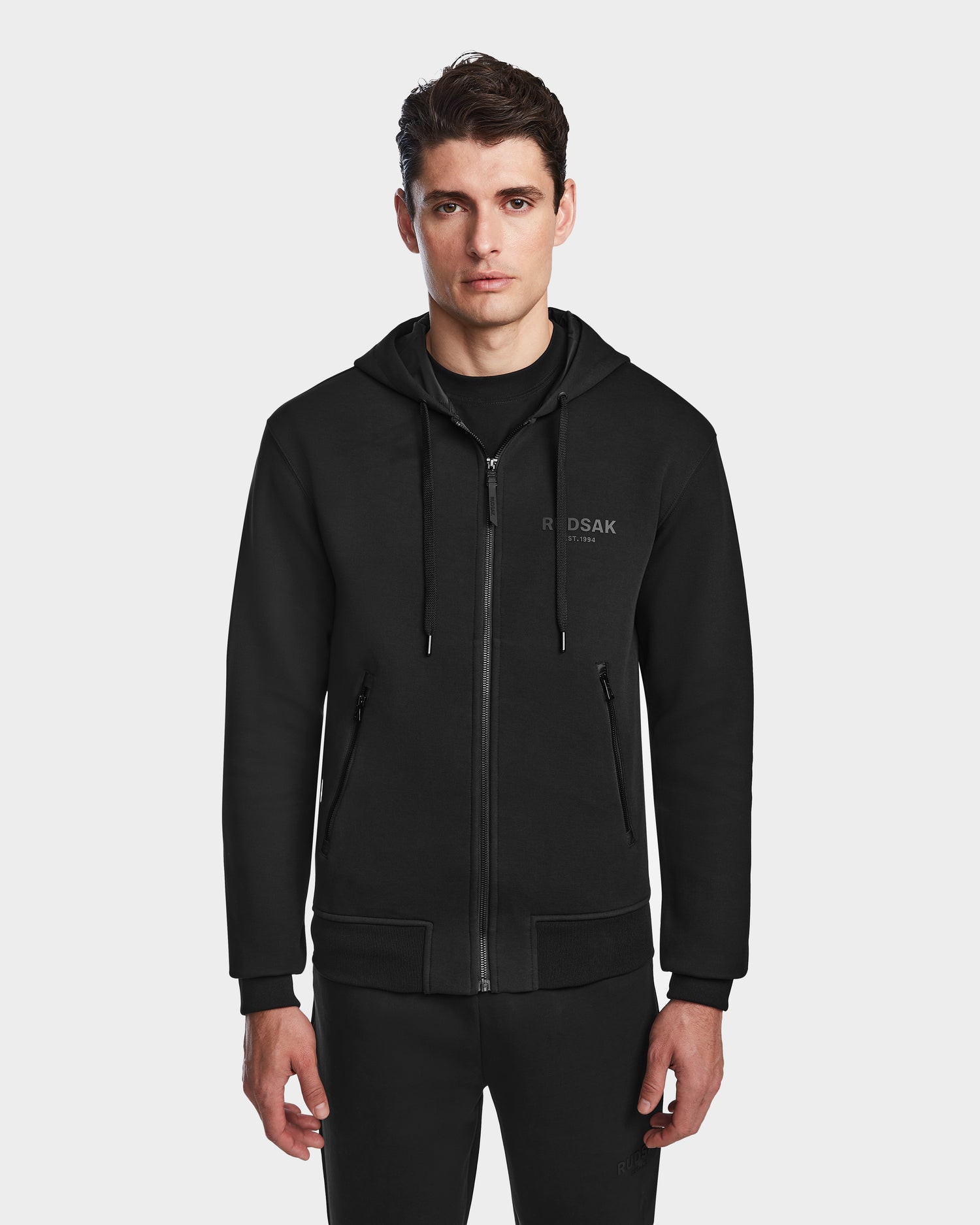 A man wearing a black Rudsak JACE - 9524010 hoodie (size M) with front pockets stands facing forward against a plain white background.