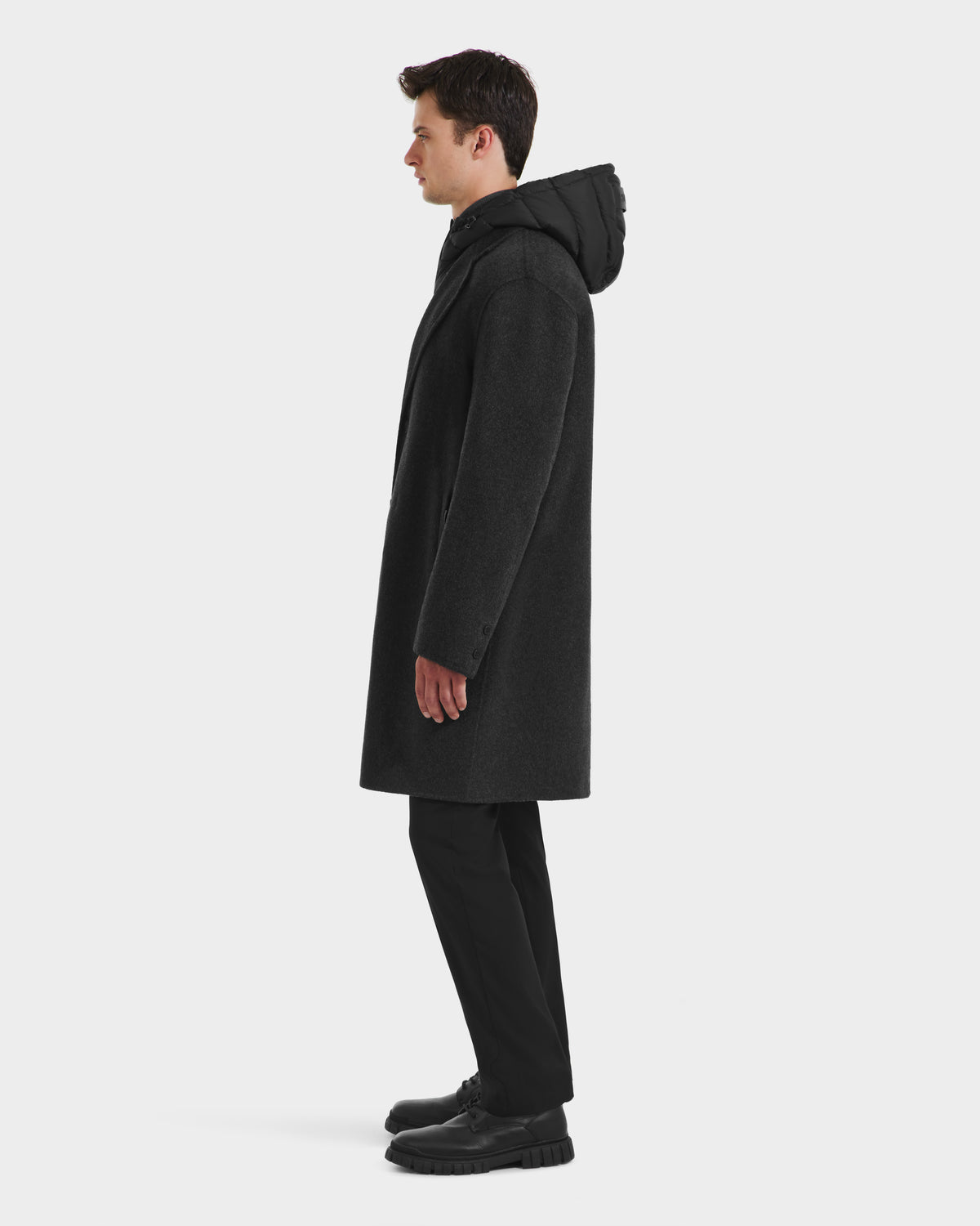 A man stands in profile wearing the Rudsak JEREMIAH - 6125509 Grey wool-blend coat with a removable down-insulated dickie, black pants, and black shoes against a plain white background.
