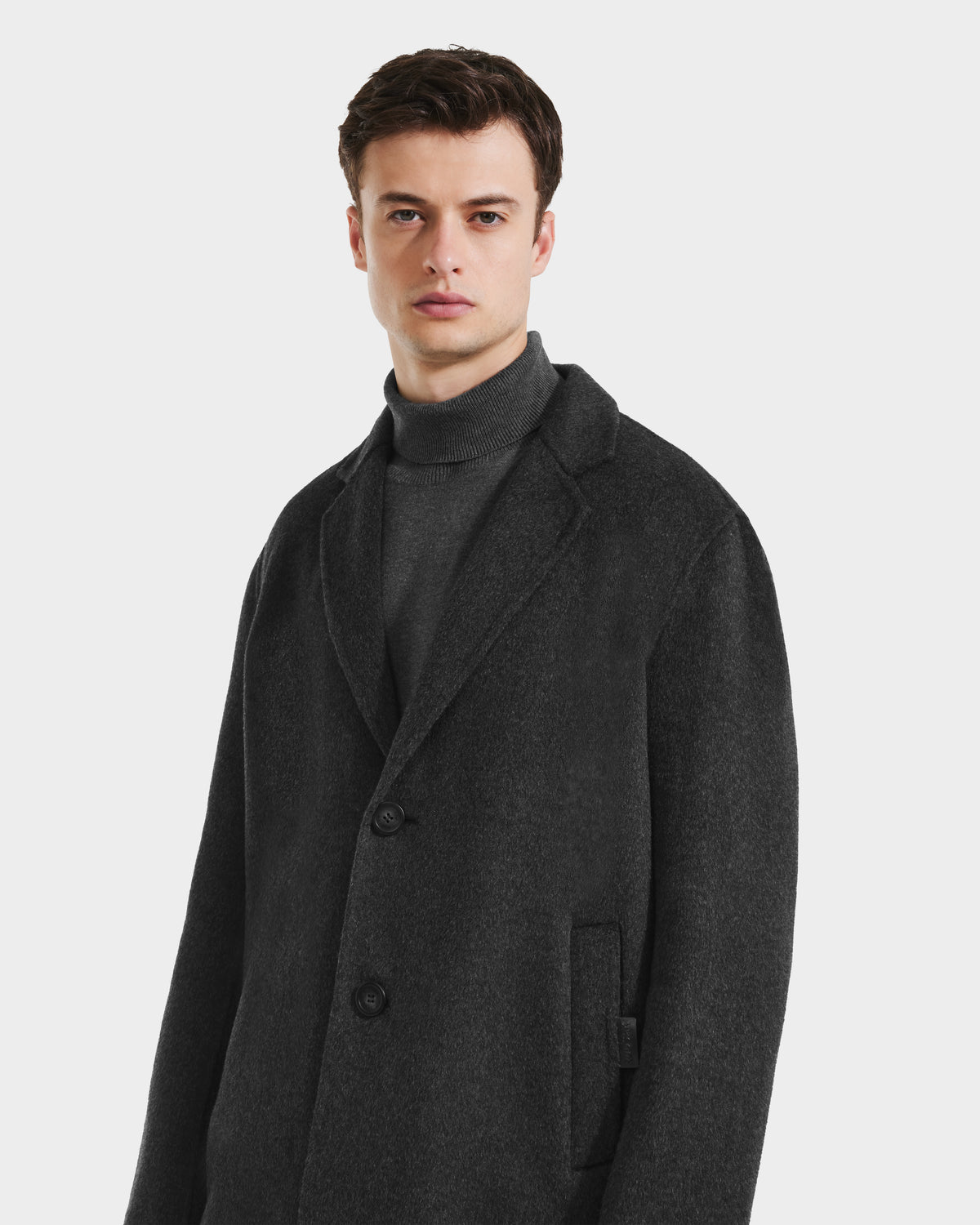 A man with short brown hair models the Rudsak JEREMIAH - 6125509 Grey men’s wool-blend coat, featuring a dark gray, buttoned style over a matching turtleneck, set against a plain light background.