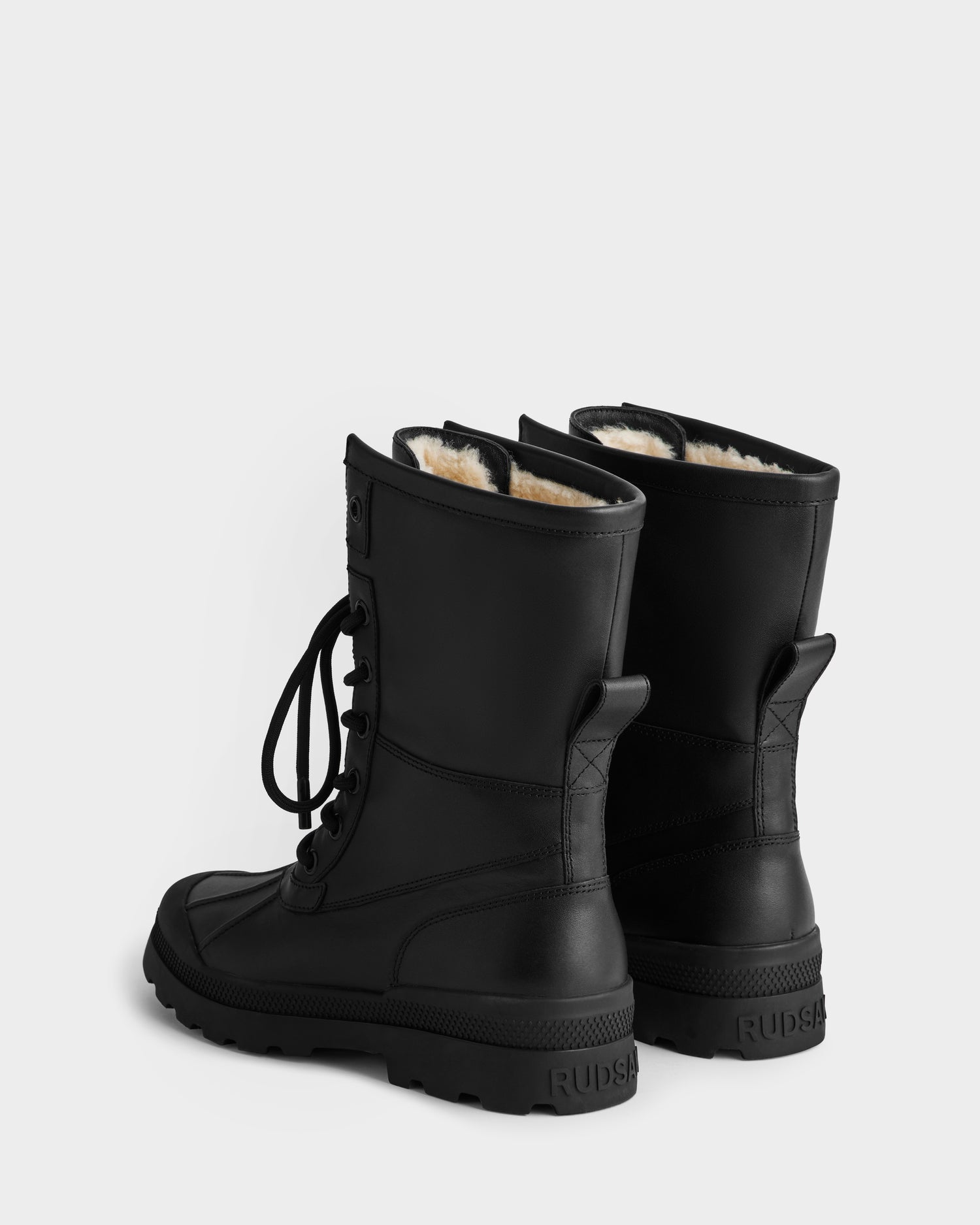 The Rudsak JESI - 8225026 Black boots feature black lace-up design, rugged soles, and light fleece lining. Shown on a white background, the boots are positioned to display their back and side views.