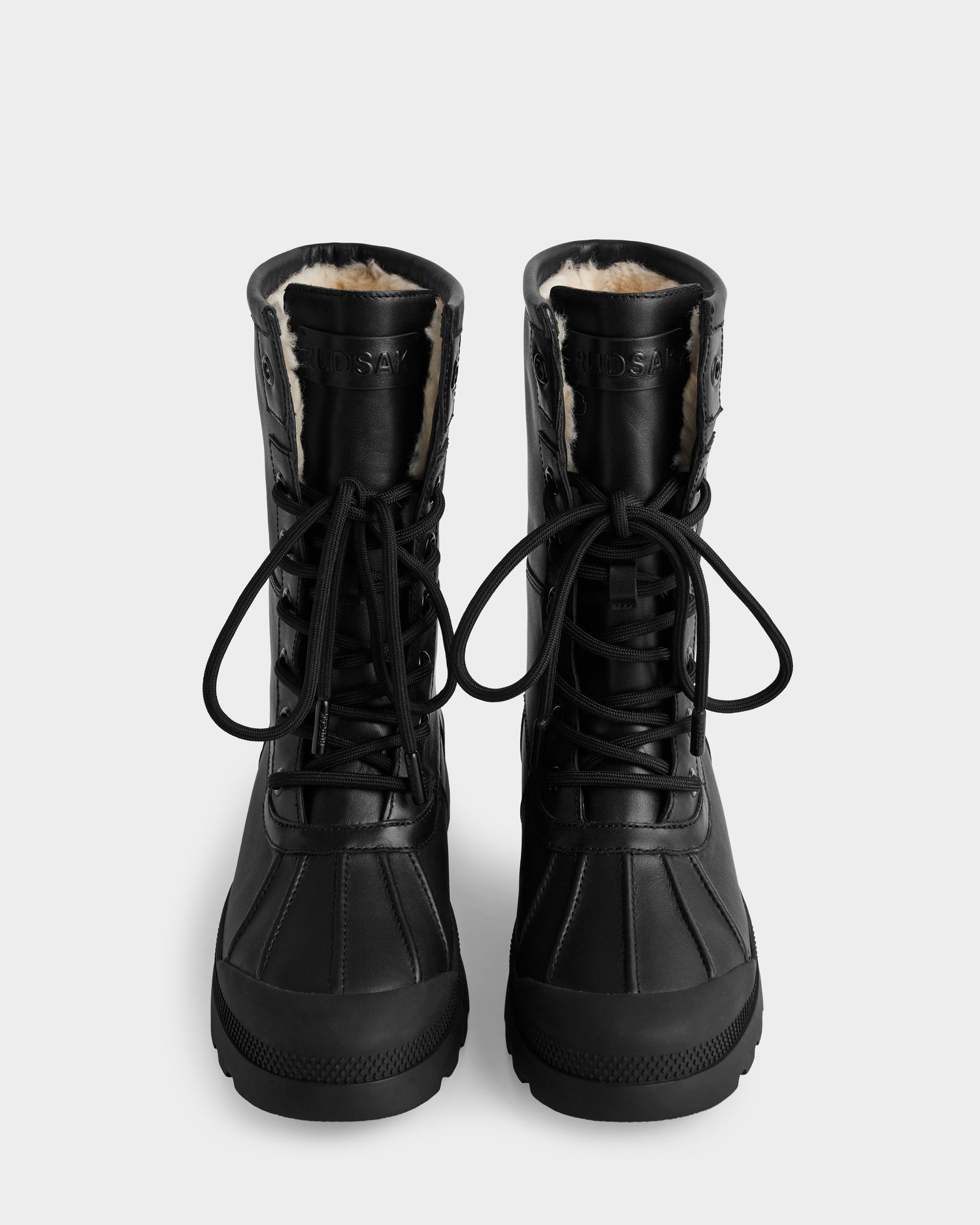 The Rudsak JESI - 8225026 Black boots are black lace-up winter boots with visible fur lining, thick rubber soles, and black laces, shown from the front against a plain white background.