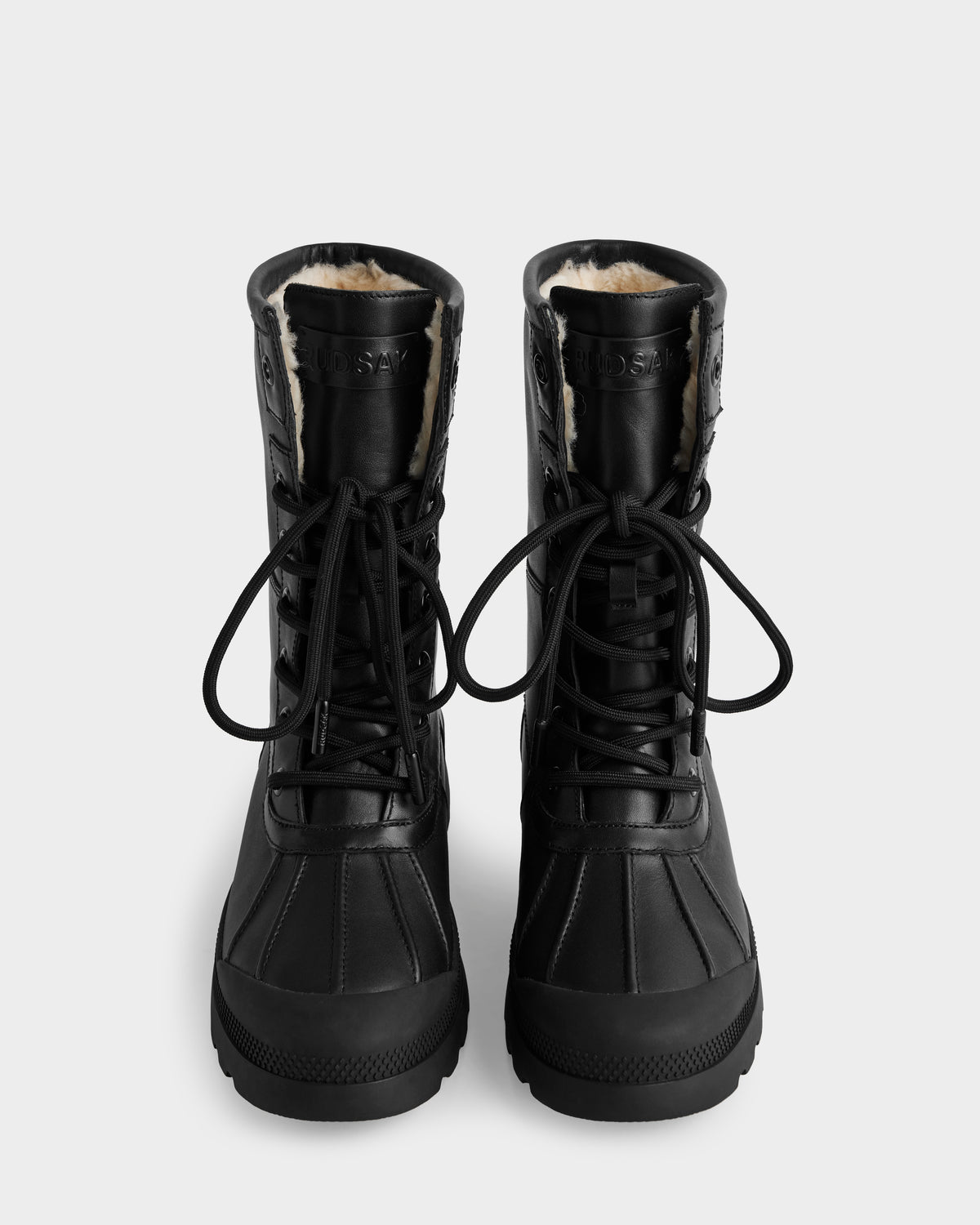 The Rudsak JESI - 8225026 Black boots are black lace-up winter boots with visible fur lining, thick rubber soles, and black laces, shown from the front against a plain white background.