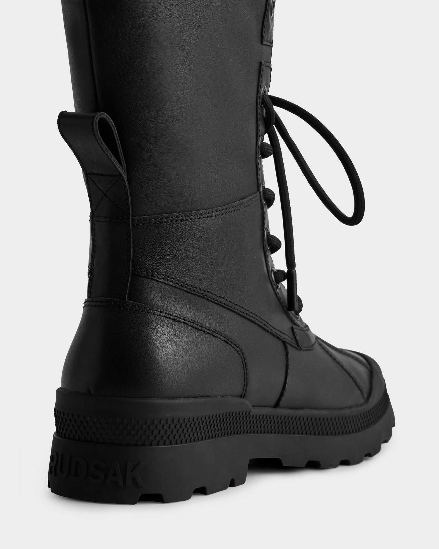 A close-up of the back and side of the black JESI - 8225026 lace-up combat boot by Rudsak, featuring a chunky sole and the brand name embossed on the heel.