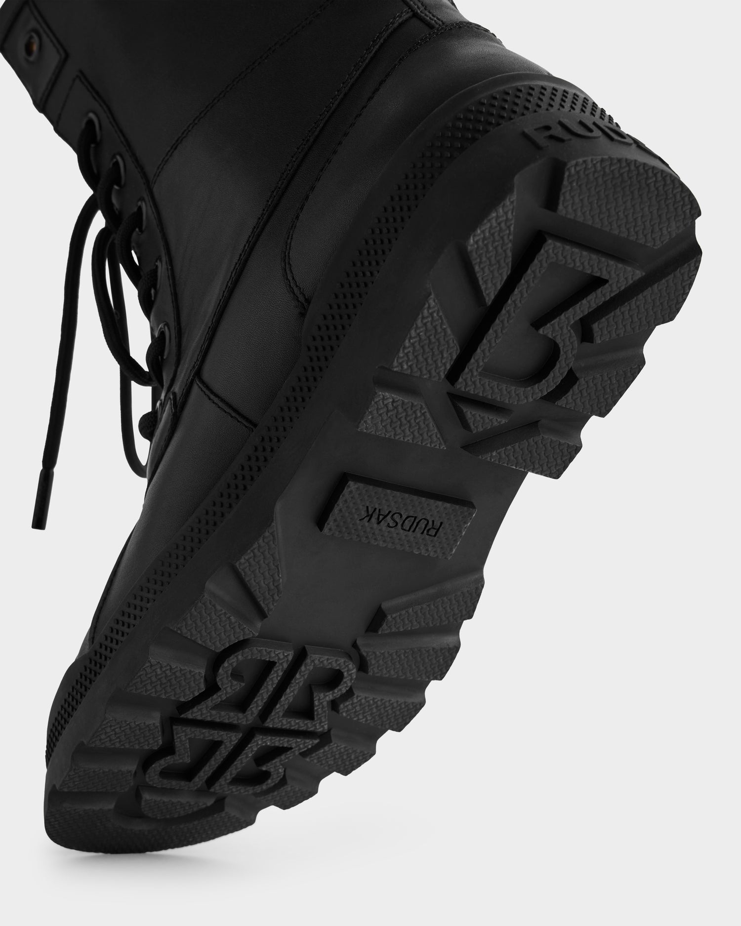 Close-up of the sole of the Rudsak JESI - 8225026 Black combat boot, featuring thick, patterned tread with embossed branding; black laces are visible on the left side.