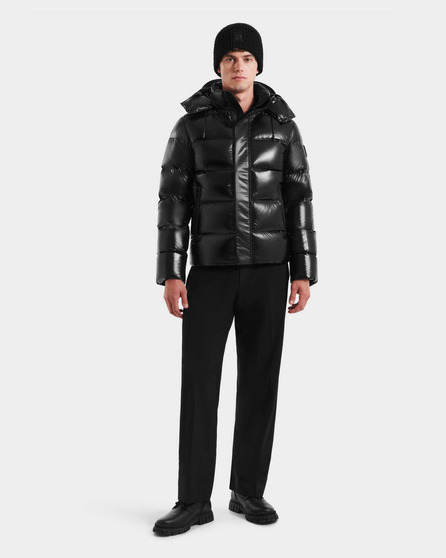 A person wearing the Rudsak JOEL S - 6124606 Black premium down puffer jacket, black beanie, pants, and shoes stands facing forward against a plain white background.