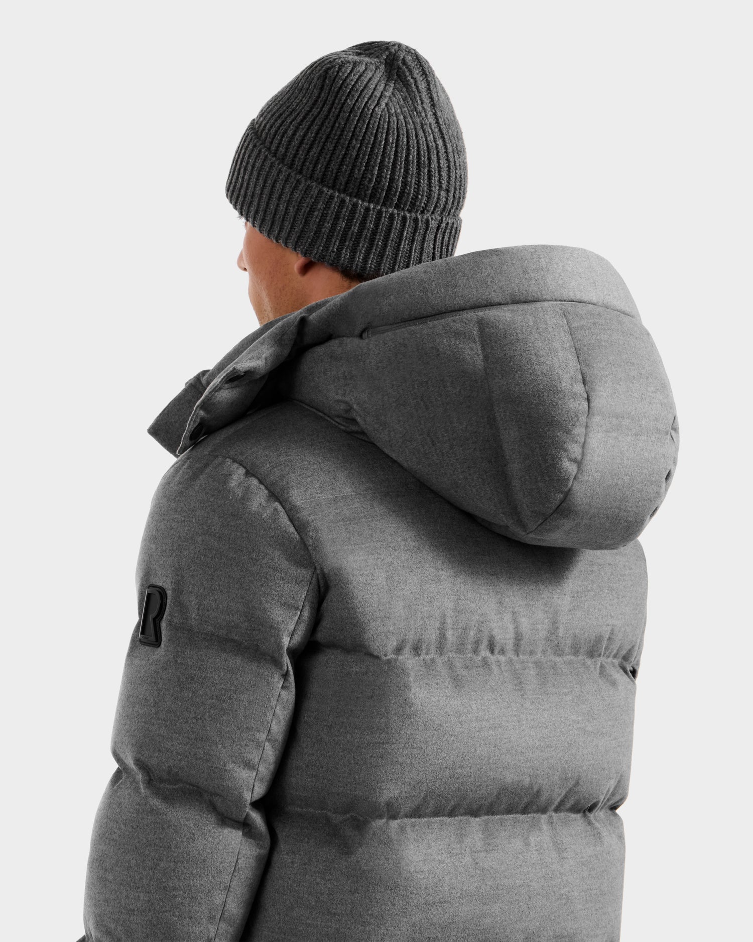 A person is seen from behind, wearing the Rudsak JOEL W - 6125683 Heather Charcoal men's wool-blend down puffer with removable hood and black sleeve patch, standing against a plain light background.