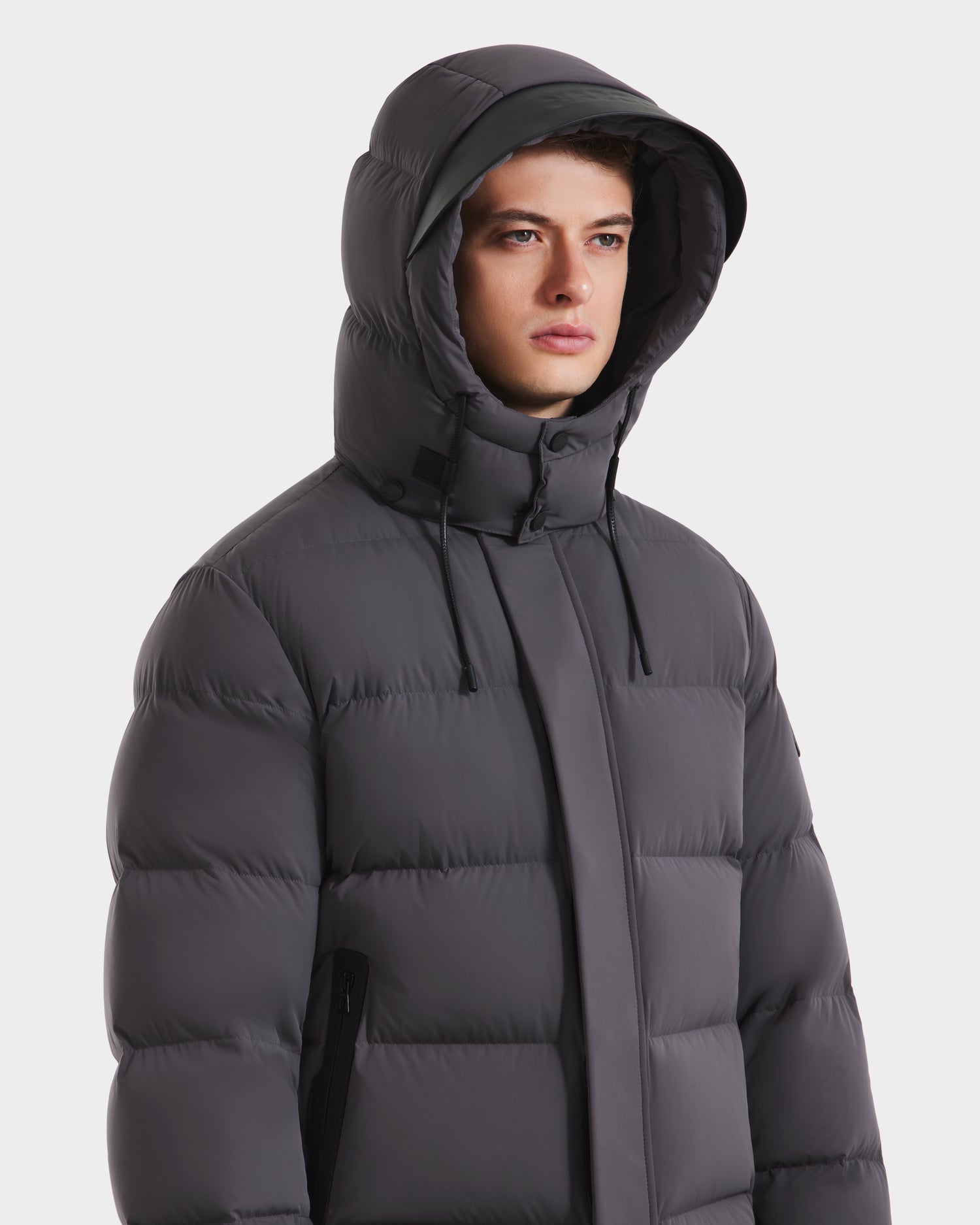 A man in a gray Rudsak JOEL - 6124605 down-filled puffer jacket stands against a white background, gazing ahead with a neutral expression.