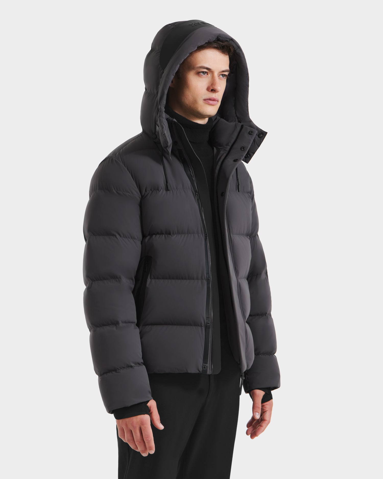 A person models the Rudsak JOEL - 6124605 Grey men's down-filled puffer jacket with black pants against a white background, looking to the side—ideal for staying warm in cold weather.