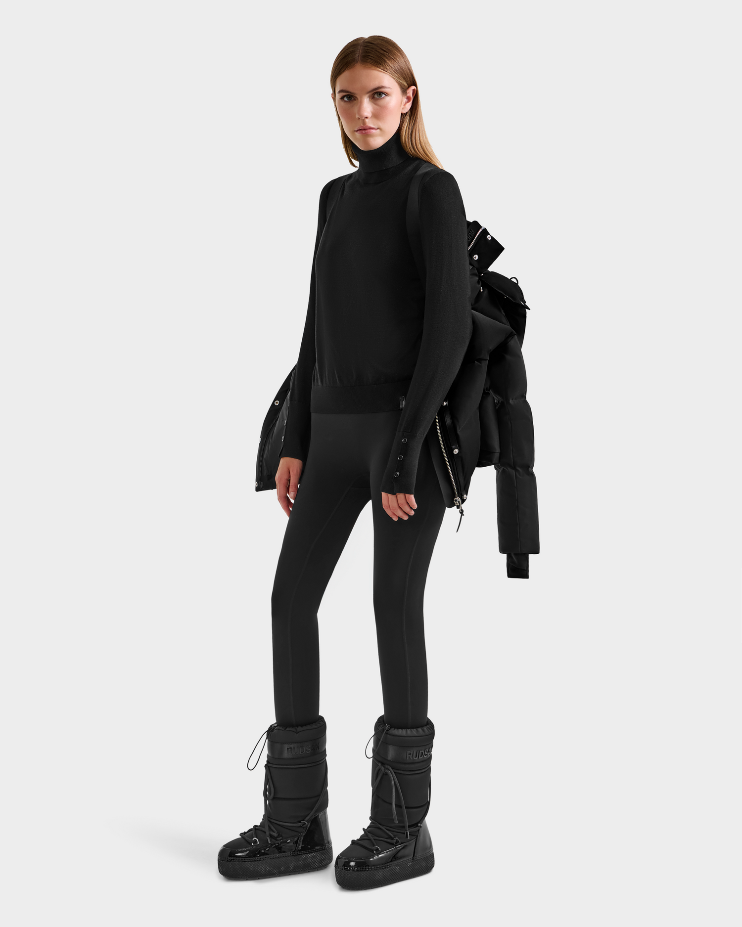 A woman poses against a plain background wearing Rudsak’s JOON H - 8125586 Black insulated winter jacket draped over her shoulders—an essential cold-weather layer.