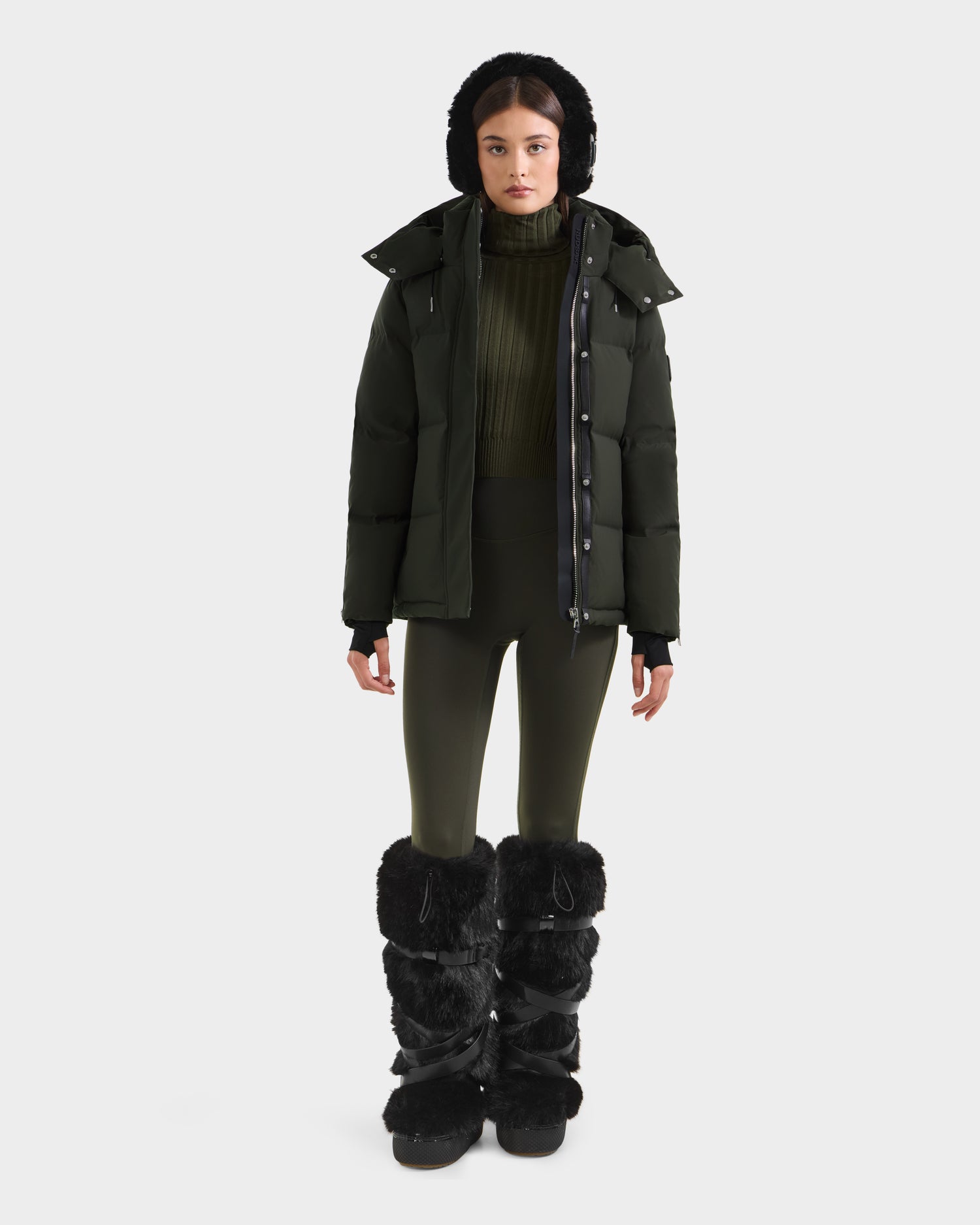 A woman stands facing forward against a plain white background, wearing the Rudsak JOON H - 8125586 Dark Olive women’s down jacket.