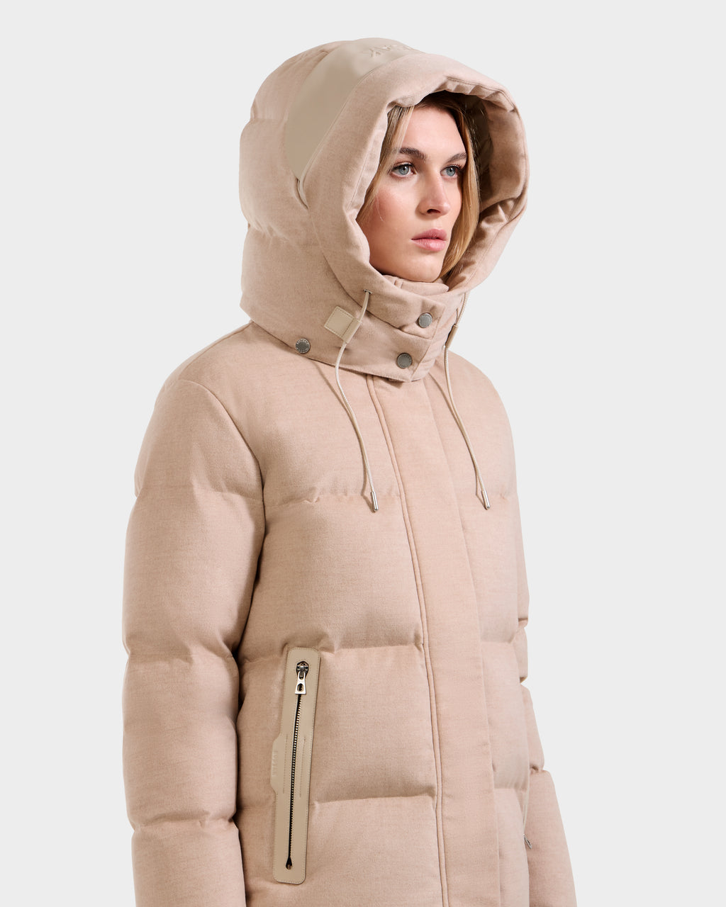 A woman models the Rudsak JOON W - 8125566 Heather Beige, a lightweight hooded puffer with zippered pockets and drawstrings, standing against a plain light background and looking slightly to the side.