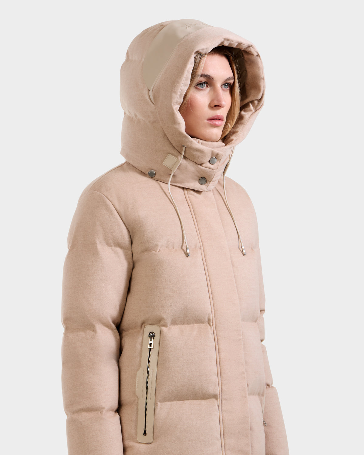 A woman models the Rudsak JOON W - 8125566 Heather Beige, a lightweight hooded puffer with zippered pockets and drawstrings, standing against a plain light background and looking slightly to the side.
