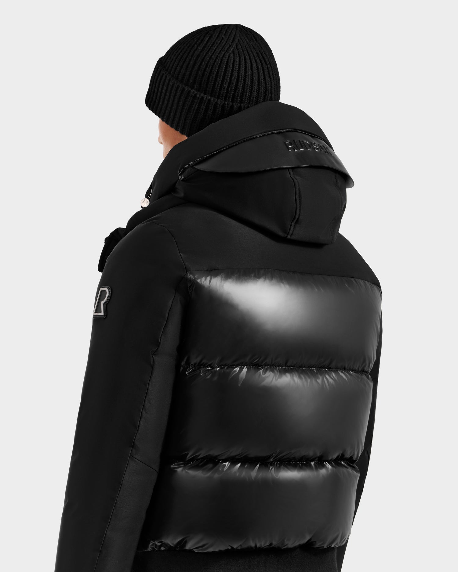 A person is seen from the back, wearing a black beanie and the Rudsak JORDY H - 6125689 Black men’s quilted down bomber with a high collar and hood, set against a plain light background.