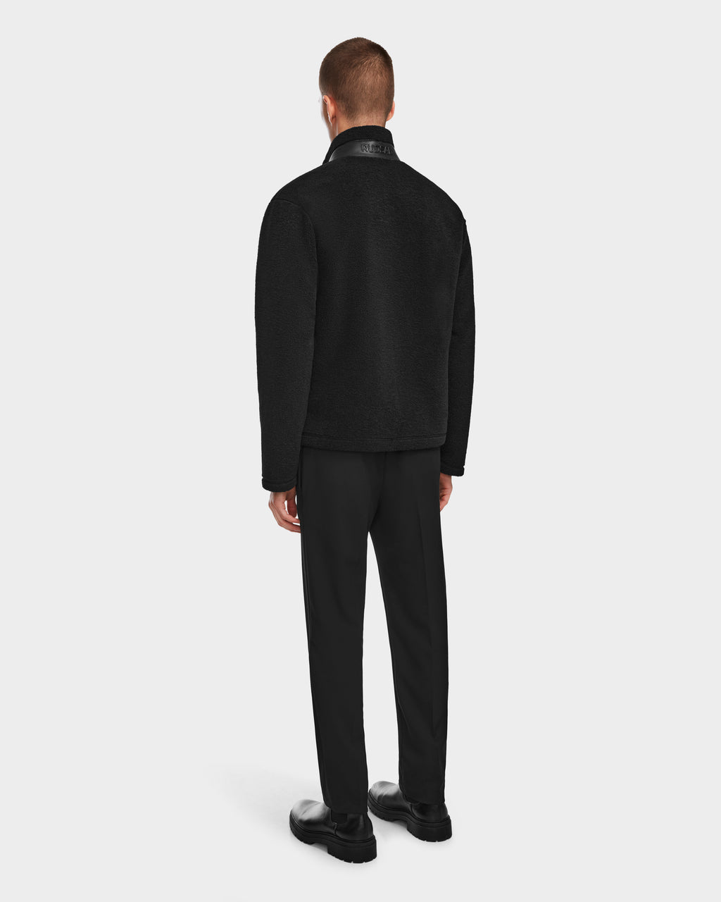 A man, seen from behind against a plain white background, wears the JOSEPH - 6524535 Black zip-up jacket and pants by Rudsak with black shoes.