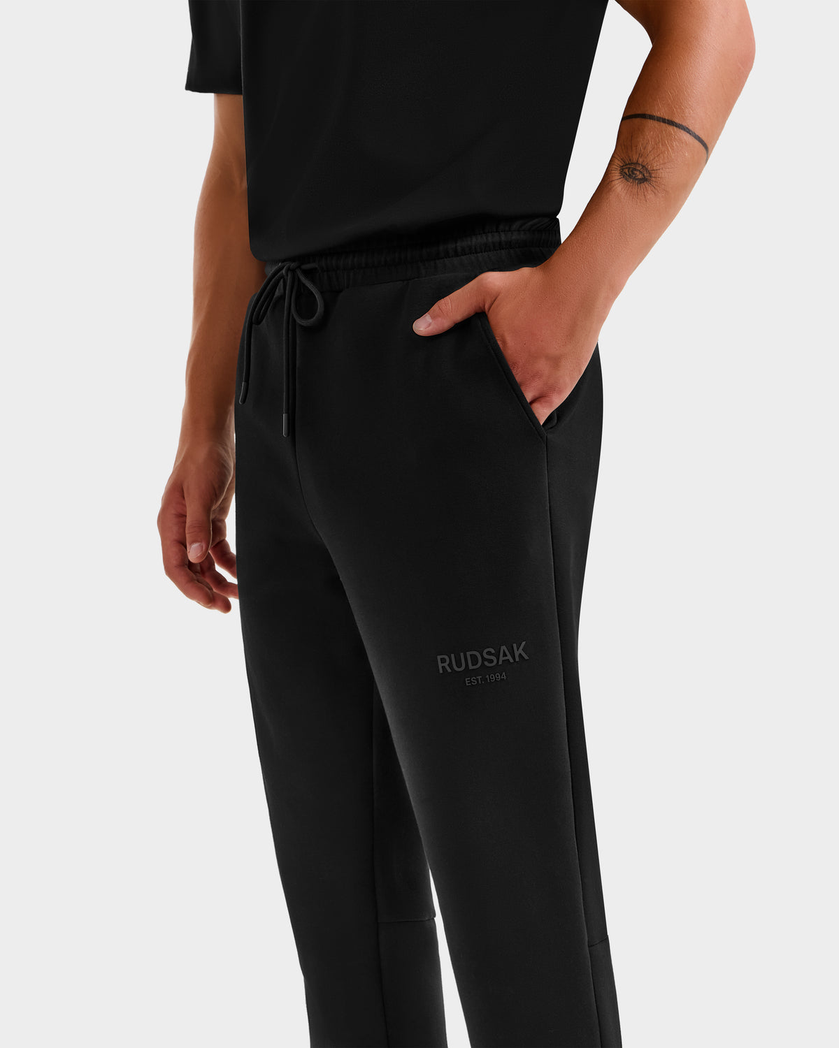 Wearing Rudsak’s JOSS - 9524009 black joggers (size M) with bold EST. 1994 print and a hand in pocket, this unisex style and a forearm tattoo create a modern, edgy look.