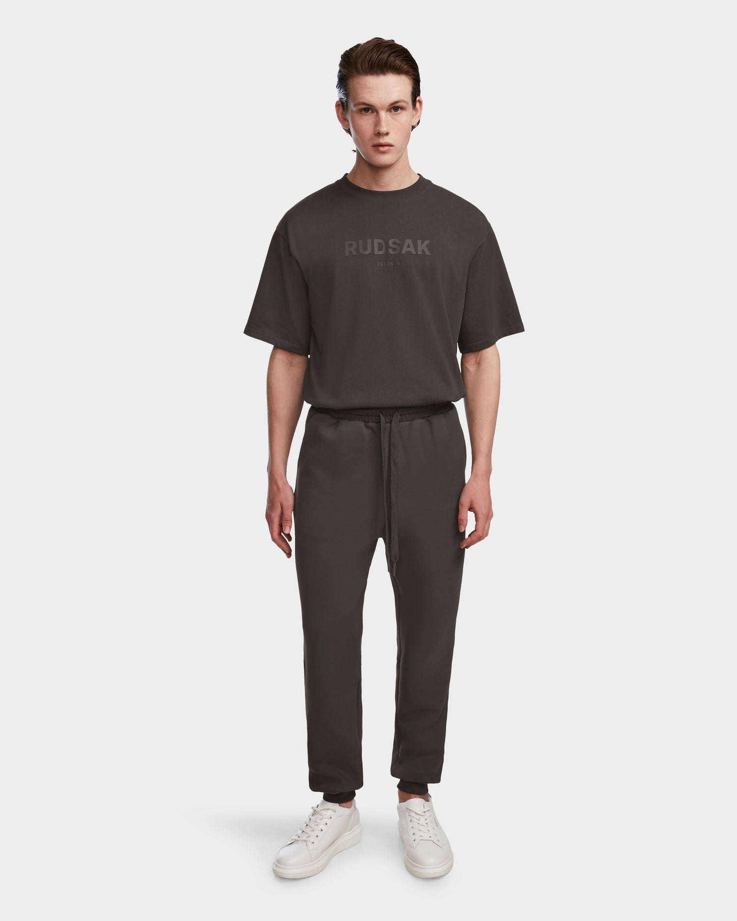 A young man stands facing forward, wearing the Rudsak JOSS - 9524009 Grey M T-shirt with matching joggers and white sneakers, set against a plain white background.