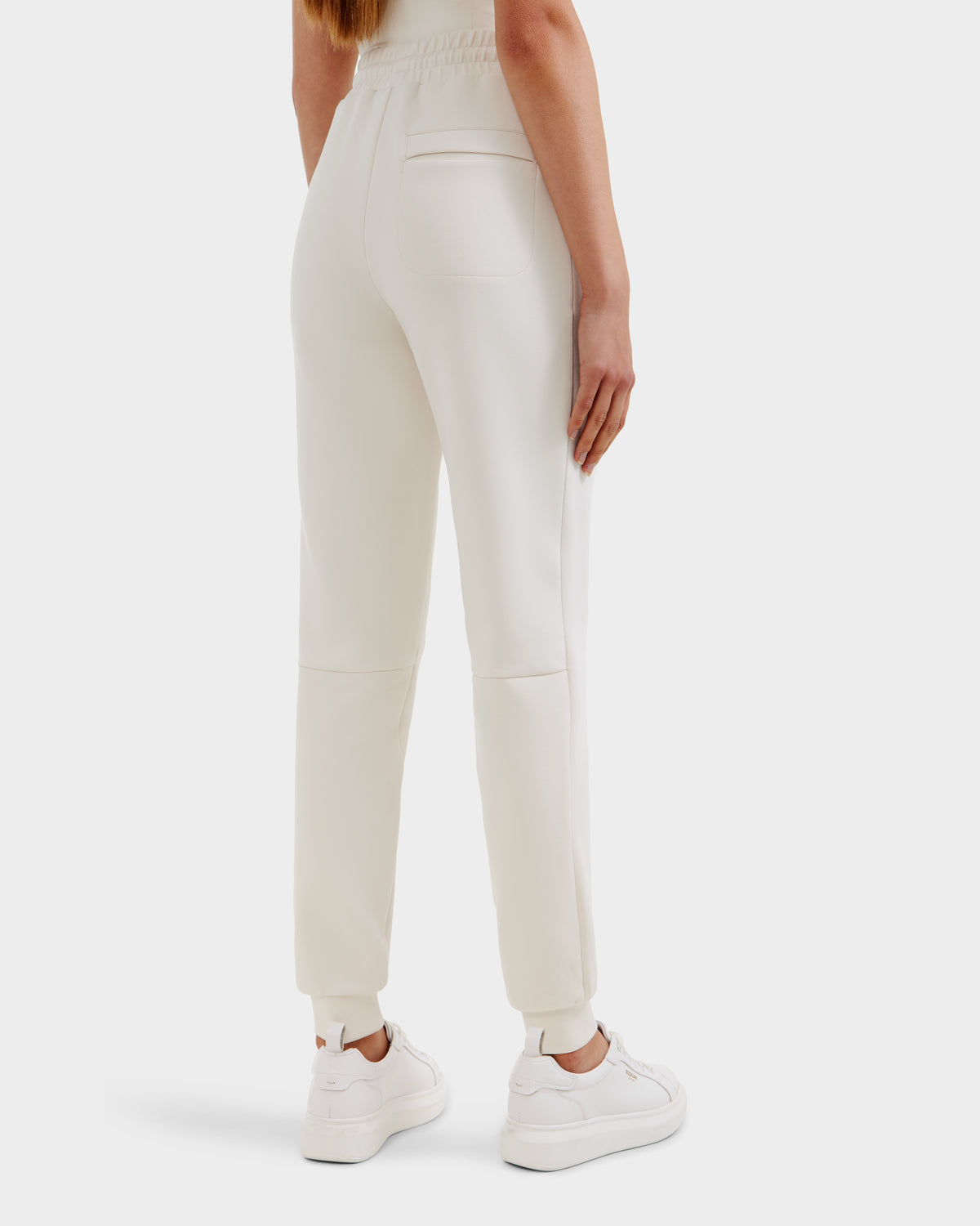 A person is seen from the back wearing Rudsak’s JOSS - 9524009 Vanilla W joggers in off-white, featuring an elastic waistband, fitted ankle cuffs, and a right pocket, styled with white sneakers.